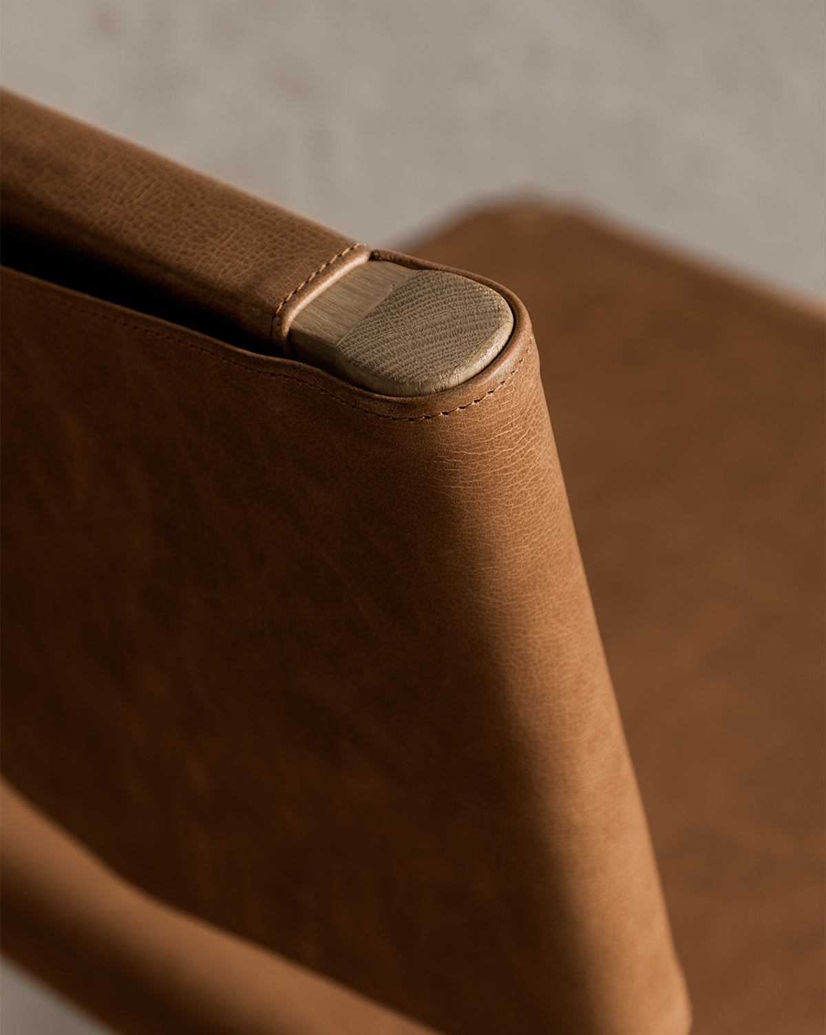 A close-up of the Danson Counter Stool highlights its brown leather seat backrest with visible stitching, elegantly wrapped around a wooden frame, set against a neutral background to showcase its minimalist design by McGee & Co.