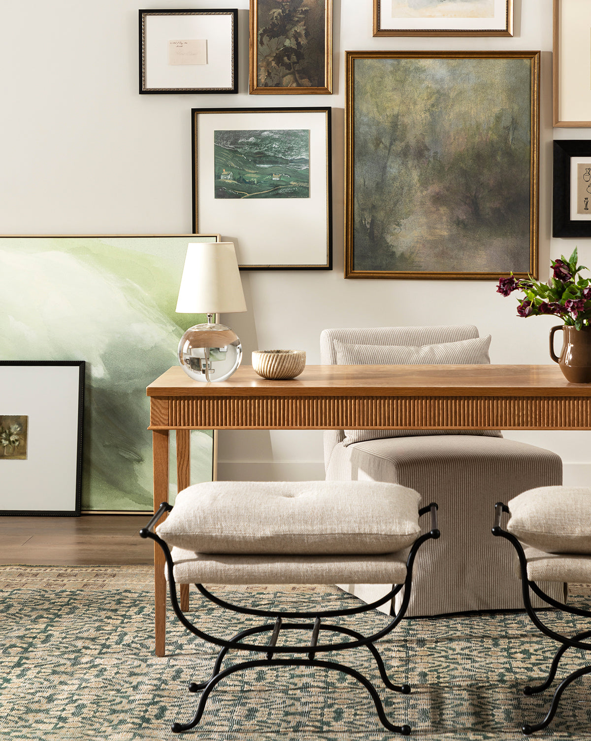 A cozy room with a wooden desk, cushioned stools, a lamp, a flower vase, framed art, neutral tones, a patterned rug, and the Beige Spiral Marble Bowl as an elegant sculptural accent, by McGee & Co.