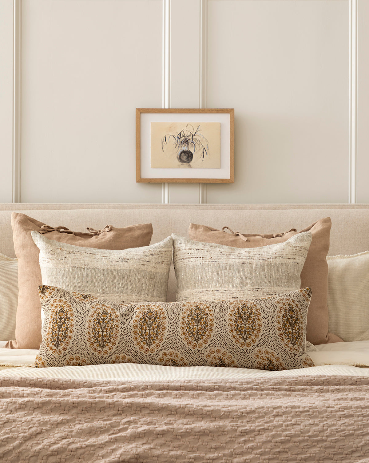 A neatly made bed features neutral pillows, a patterned bolster, and above it hangs Willow Branches, a framed botanical still life print, all set against a light-paneled wall for a soft, calming look.