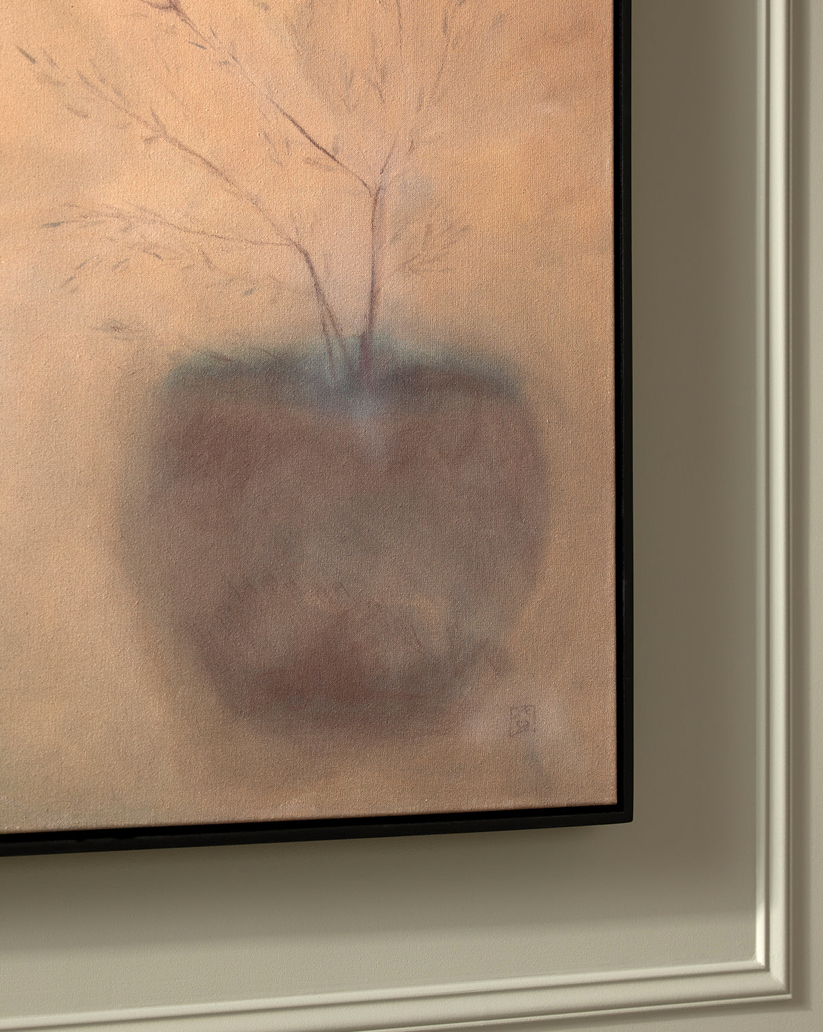 A close-up of Olive by Jess Engle: a framed abstract painting of a potted plant with thin branches on a soft beige background, hanging on a wall with decorative molding in an American maple frame.