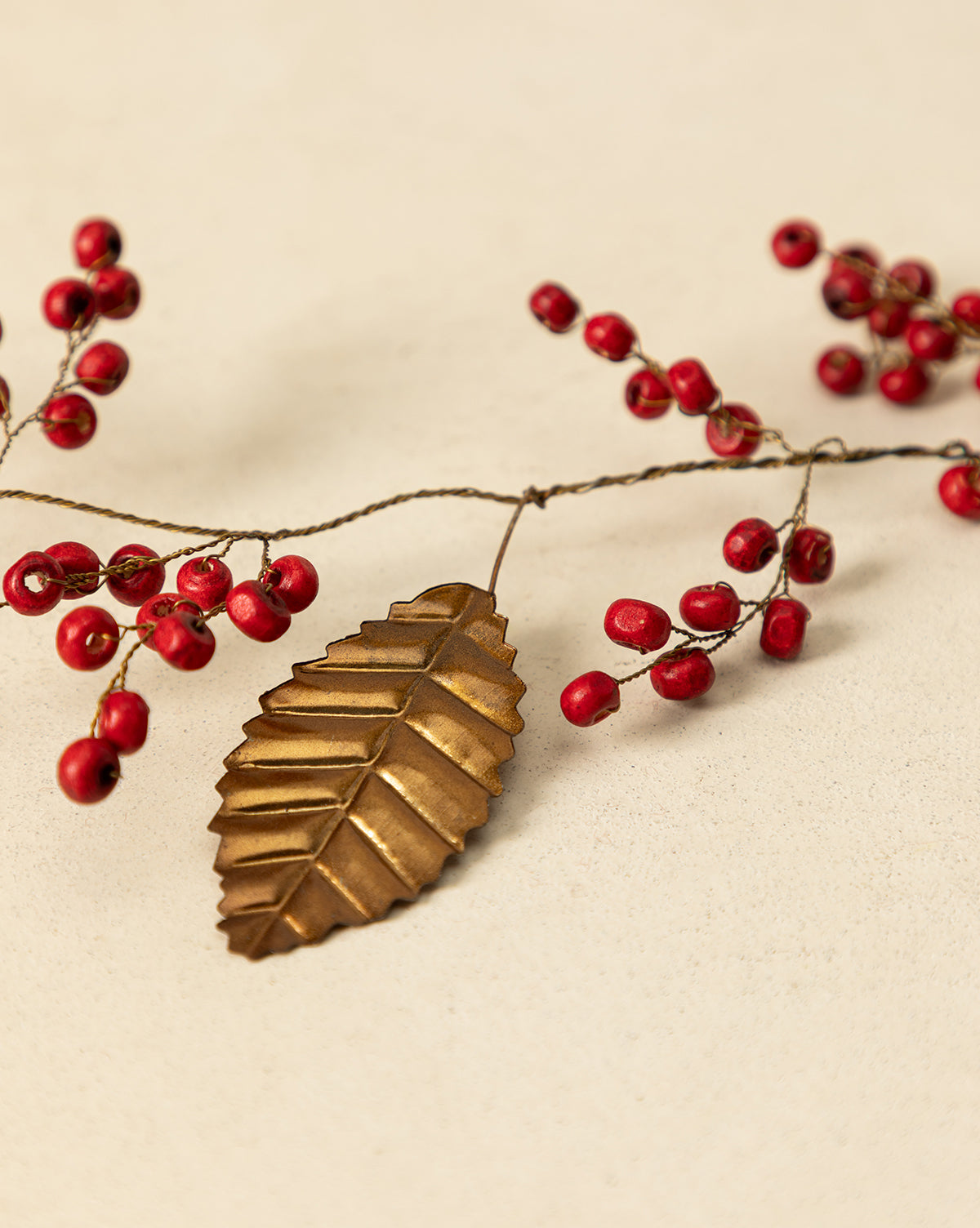 The 6' Holly Berry Garland, featuring metallic gold leaves and red berry sprigs, creates a simple yet elegant festive décor, perfect as a holiday accent on any light beige surface, by McGee & Co.