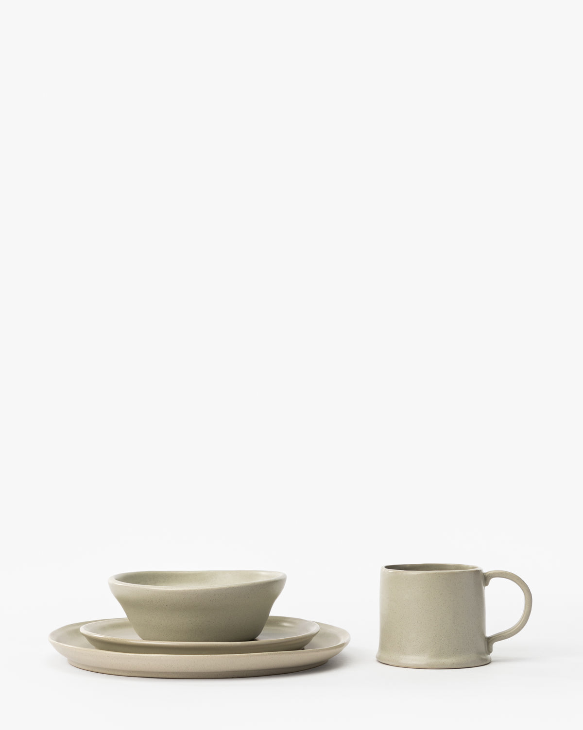 The Aiden Soft Gray Side Plate, in a minimalist design, is showcased with a classic round plate, mug, bowl, and stacked plates, all arranged neatly against a plain white background in soft gray tones, by McGee & Co.