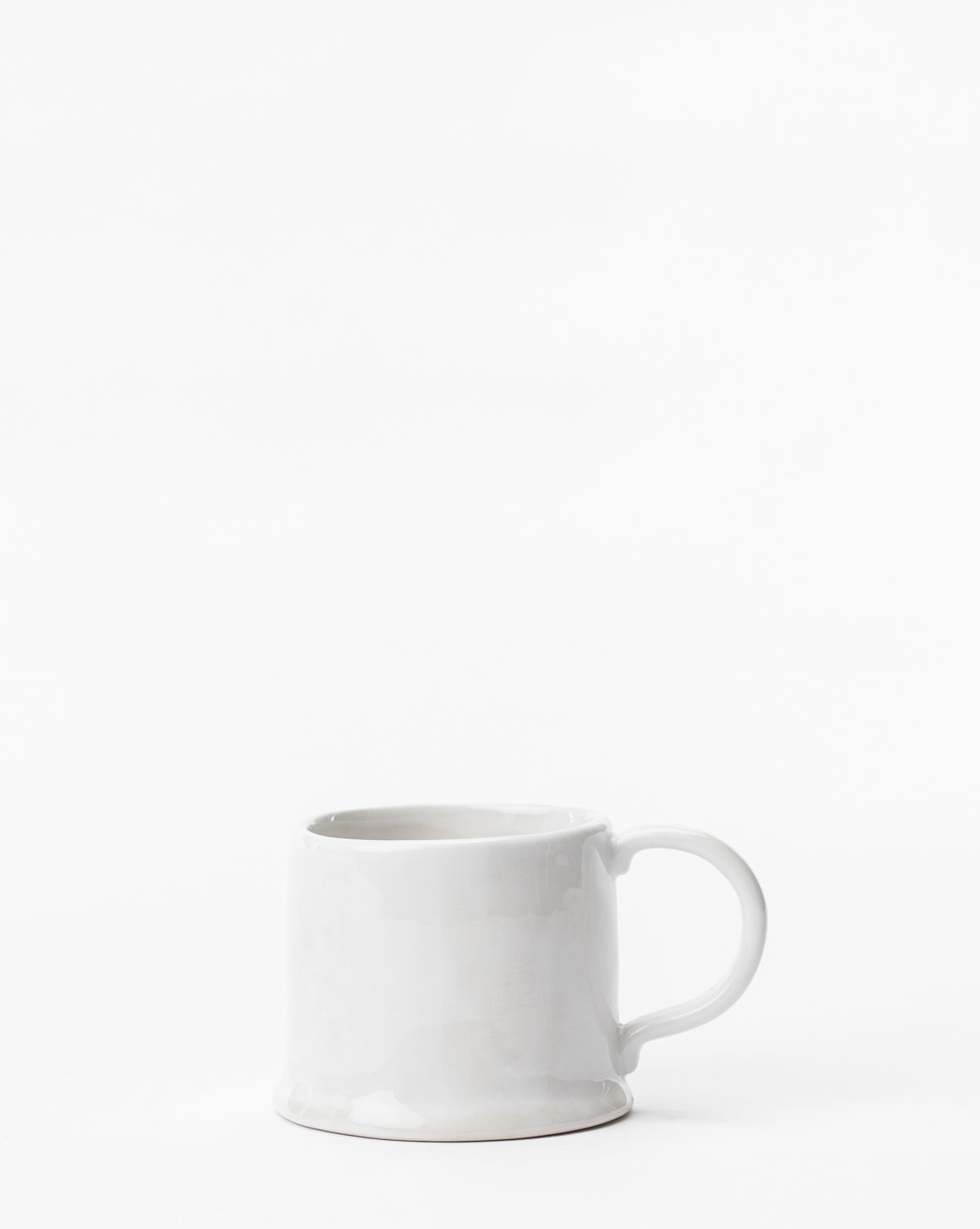 The Aiden Mug, a modern white ceramic mug, rests on a white surface—a stylish piece of dinnerware in a minimalist setting, by McGee & Co.