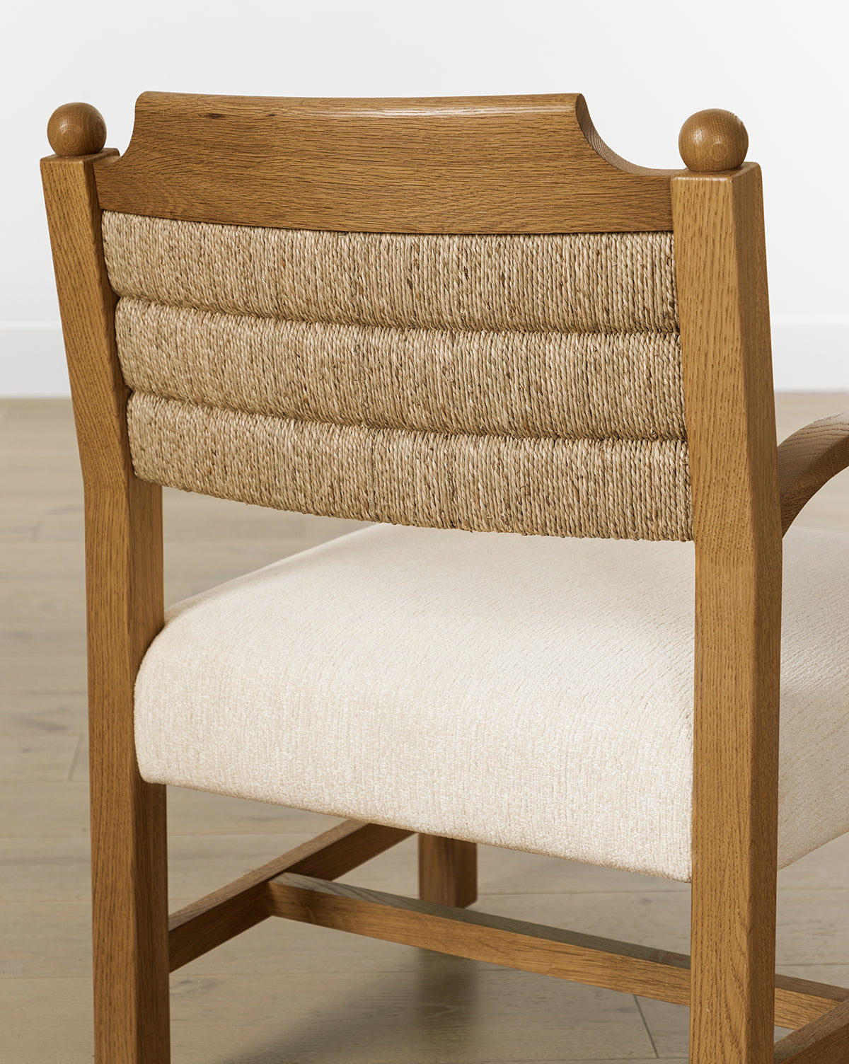 The Alberta Lounge Chair features a vintage-inspired design with a rope-wrapped backrest and cushioned cream seat, shown on a light wood floor against a white wall by McGee & Co.