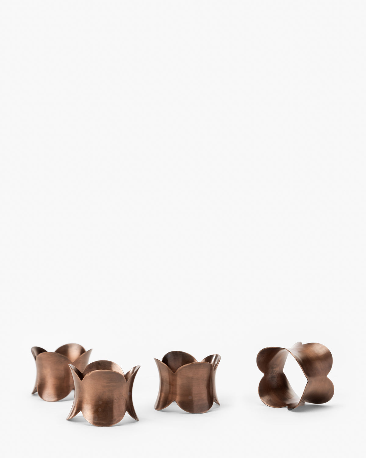 The Alina Napkin Rings (Set of 4) feature curved, petal-like brass edges and are arranged on a white surface, highlighting their sculptural shapes and bringing elegant style to any table setting, by McGee & Co.