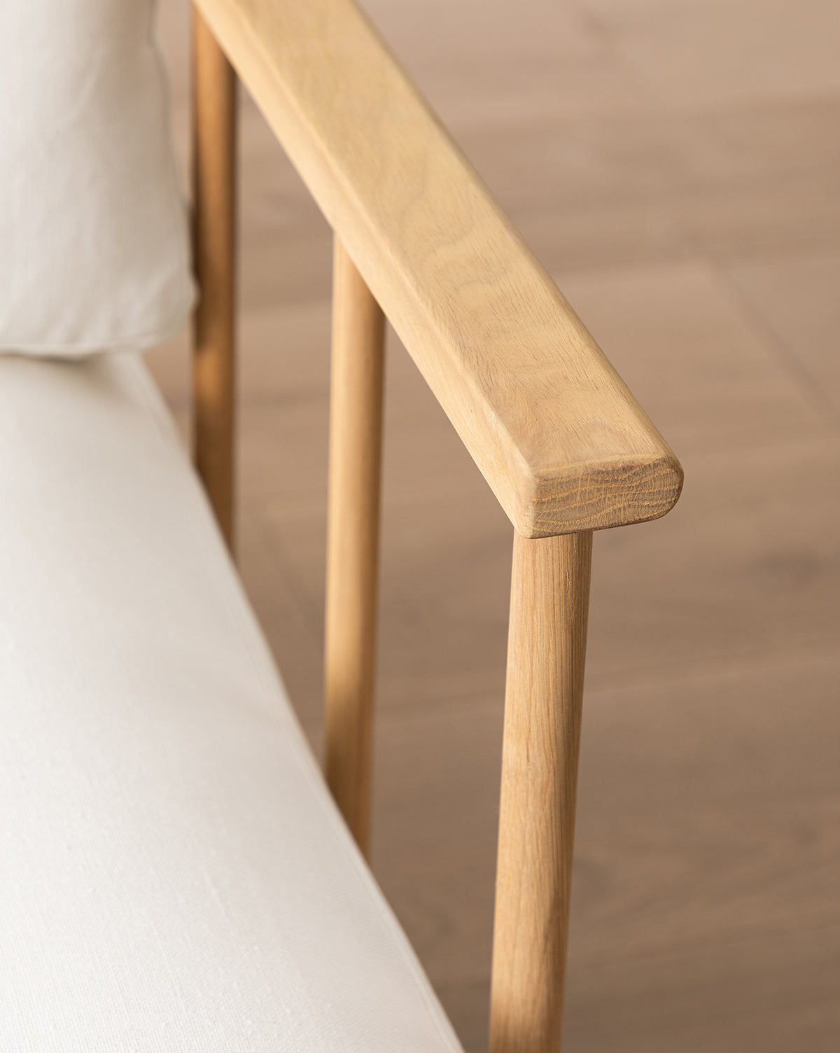 Close-up of the Alma Lounge Chair, crafted from solid oak with a light wooden armrest and backrest, plus a comfortable cushion, set on a wooden floor background by McGee & Co.