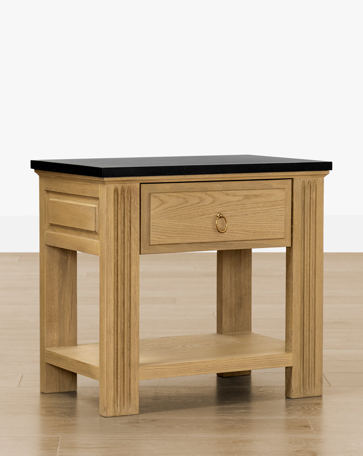 The Ambrose Nightstand features a honed granite top, single drawer with brass ring handle, paneled sides, and a lower shelf, by McGee & Co. Shown on a light wood floor against a plain white background—ideal vintage-style bedroom furniture.