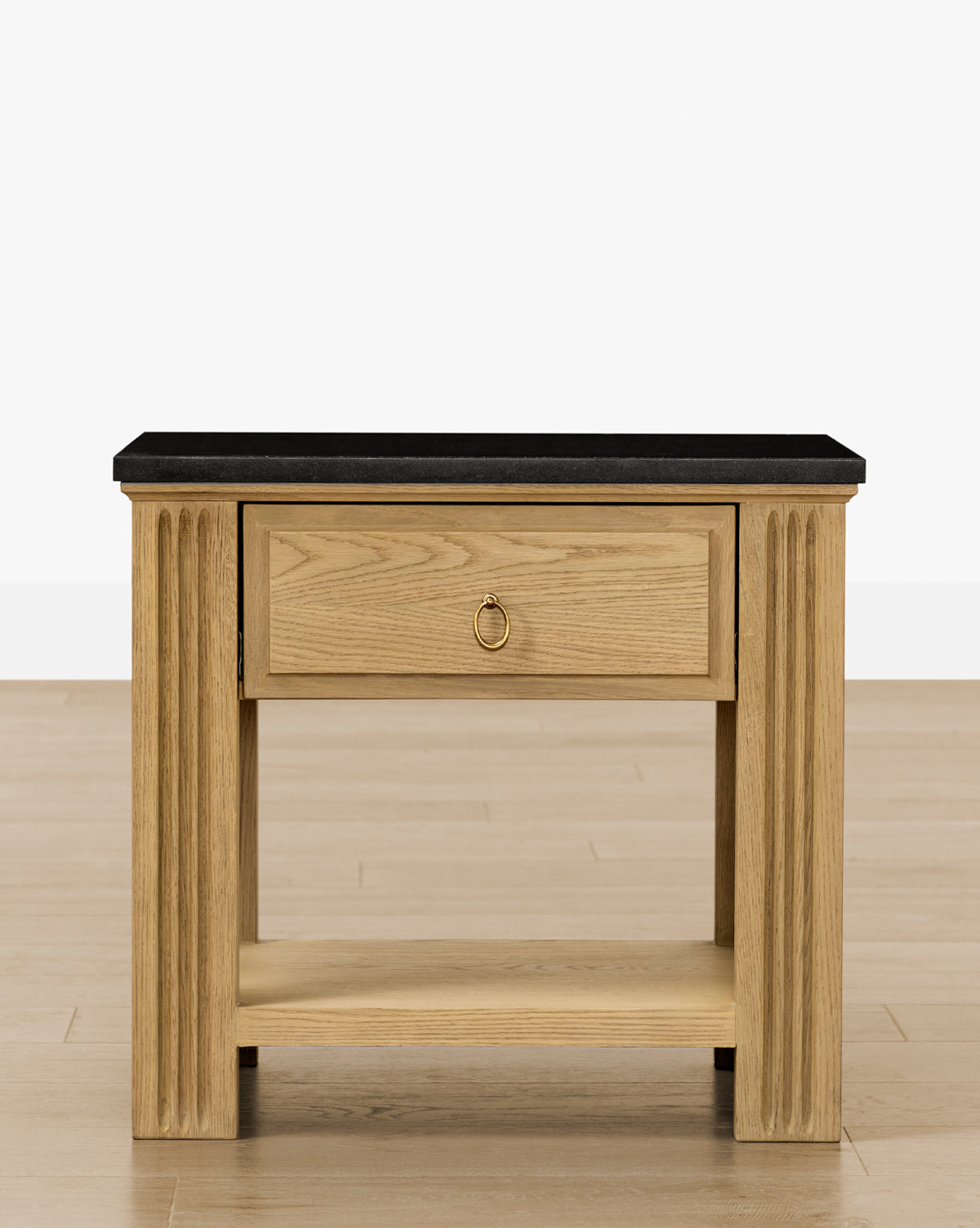 The Ambrose Nightstand features fluted legs, a single drawer with a round metal pull, a honed granite top, and an open bottom shelf—ideal for vintage bedroom decor—shown on light wood flooring against a white background by McGee & Co.