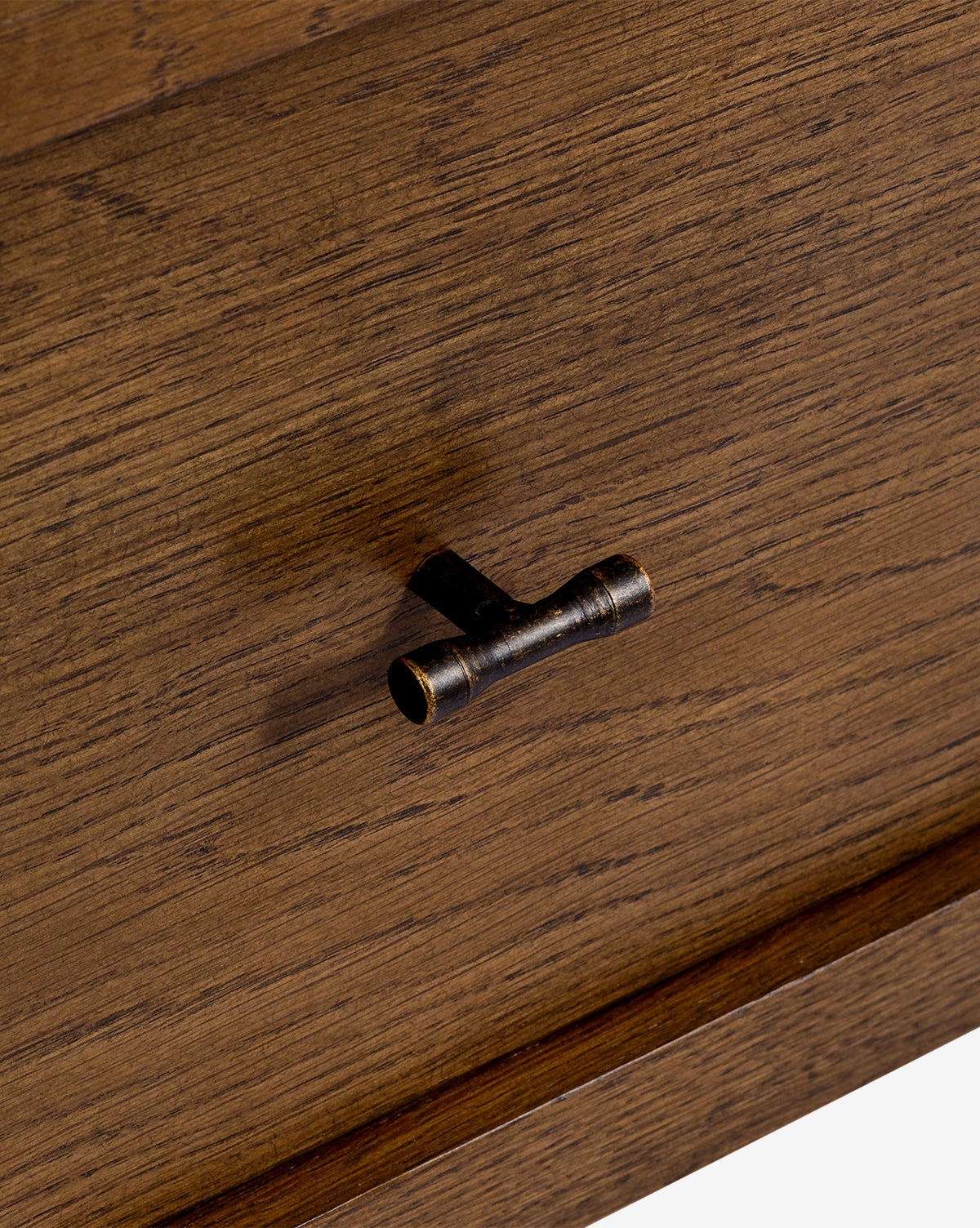 Close-up of the Ambrosia Nightstand drawer featuring a cylindrical antique brass handle, mounted horizontally on the walnut oak veneer front with a natural brown grain texture, by McGee & Co.