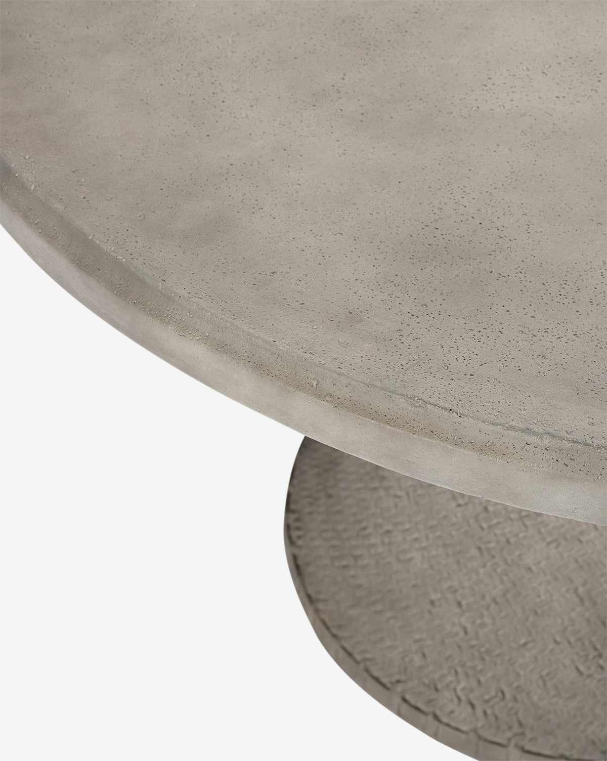 Close-up view of the Andrea Dining Table, showcasing its smooth, slightly textured stonecast surface and a portion of the patterned cylindrical base by McGee & Co.