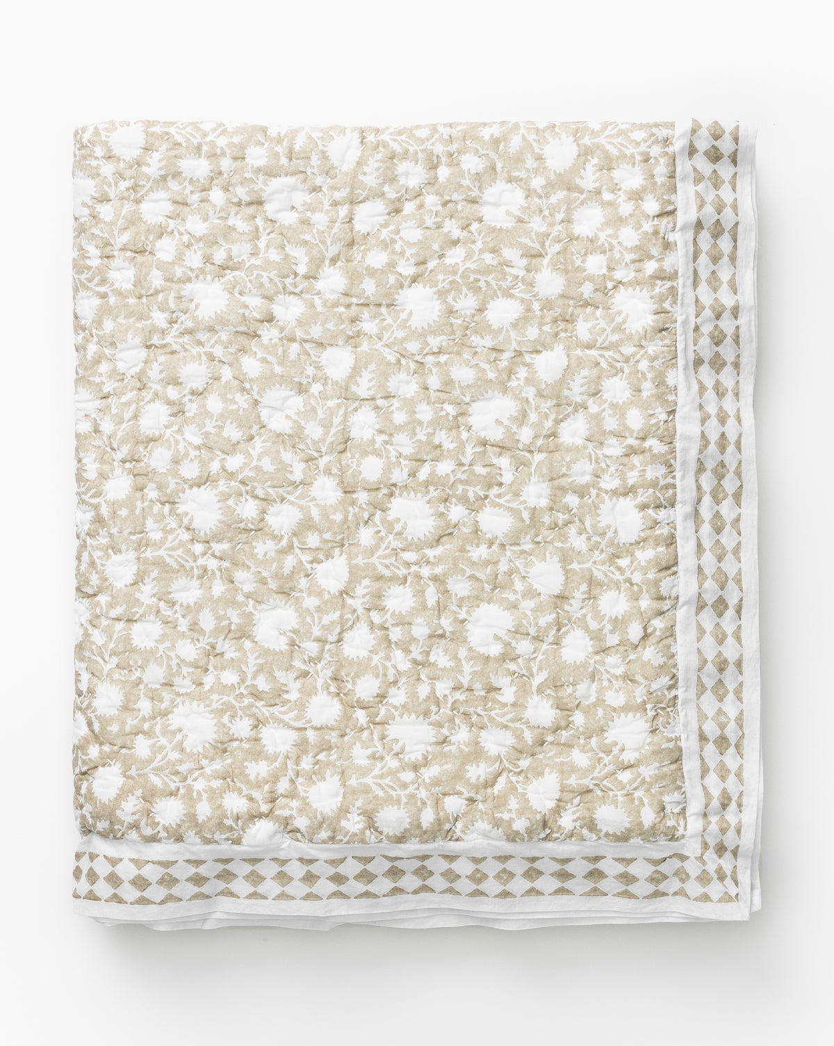 The Arcadia Block Print Kids Quilt features a folded floral quilt with a beige pattern on white and a geometric diamond border, perfect for brightening up any kids room.