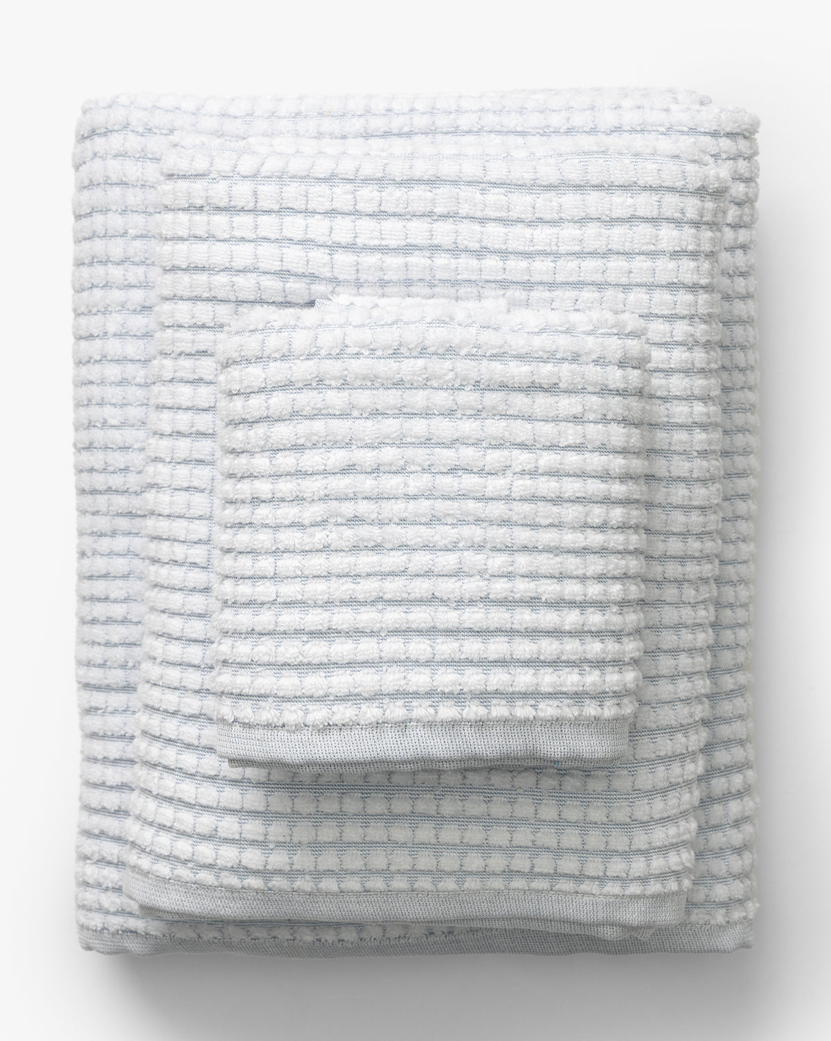Two gray waffle weave towels from our Atrani Gray Organic Bath Collection are neatly folded and stacked on a plain white background. Made from organic cotton, the smaller towel sits elegantly atop the larger one, by McGee & Co.