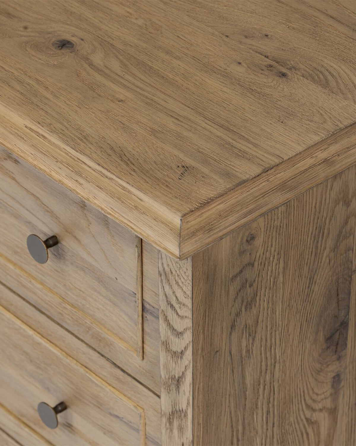 A close-up of the Aurelian Nightstand’s top corner showcases its three drawers with round metal knobs and natural smoked oak grain finish—ideal for chic bedroom storage, by McGee & Co.