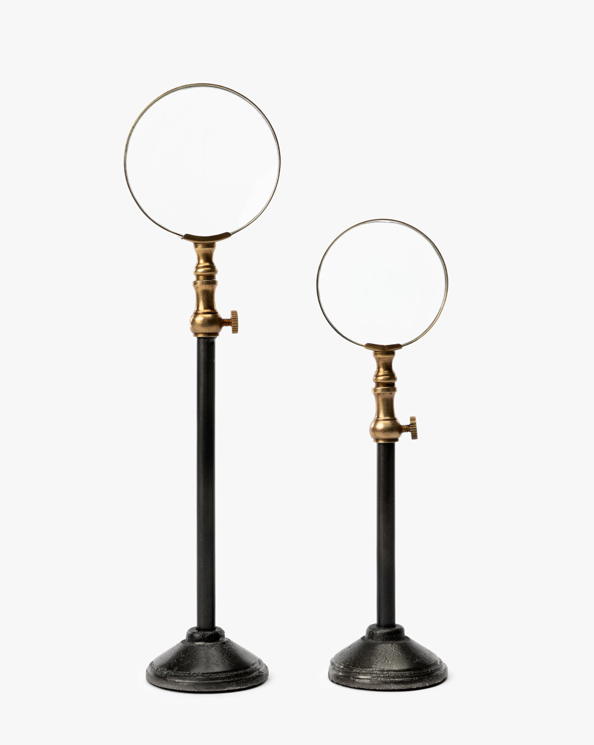 The Barnabas Standing Object features two vintage-style magnifying glasses with burnished brass fittings on tall black metal stands with round bases—a timeless accent for your home decor, shown against a plain white background, by McGee & Co.