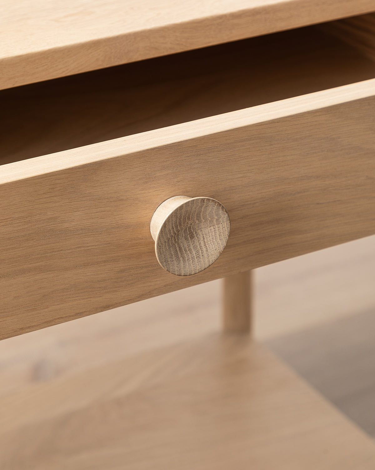A close-up of the Baxter Nightstand shows its light wood drawer, partially open, with a round wooden knob. Visible wood grain and a smooth finish highlight this transitional design bedroom furniture piece, by McGee & Co.