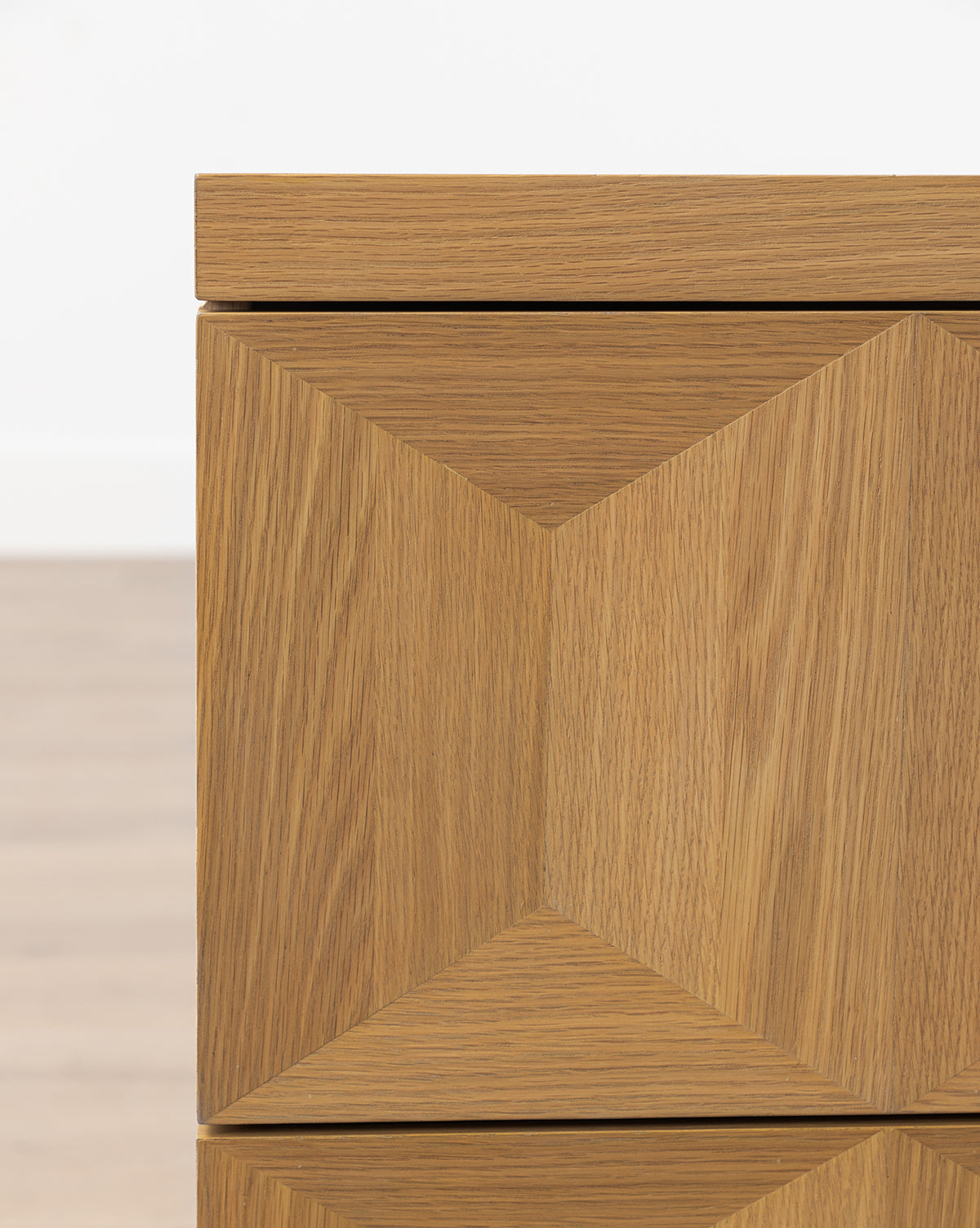 Close-up of the Beacon Nightstand’s white oak corner, showcasing a geometric diamond pattern on the front, natural wood grain, and light brown finish, by McGee & Co.