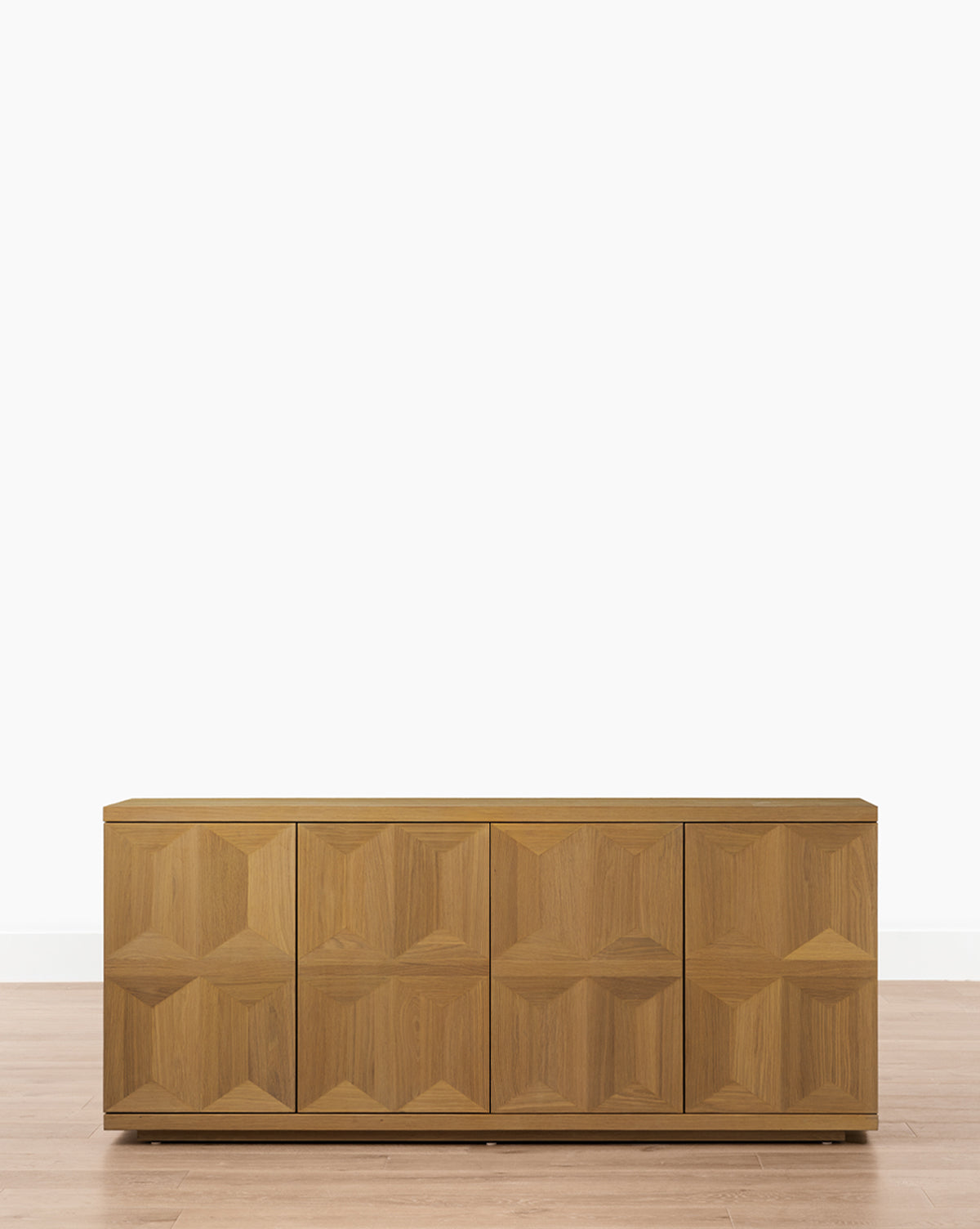 The Beacon Sideboard, crafted from natural materials, has four doors with geometric carvings. This spacious cabinet stands on a flat base and is shown against a white background on a light wood floor by McGee & Co.