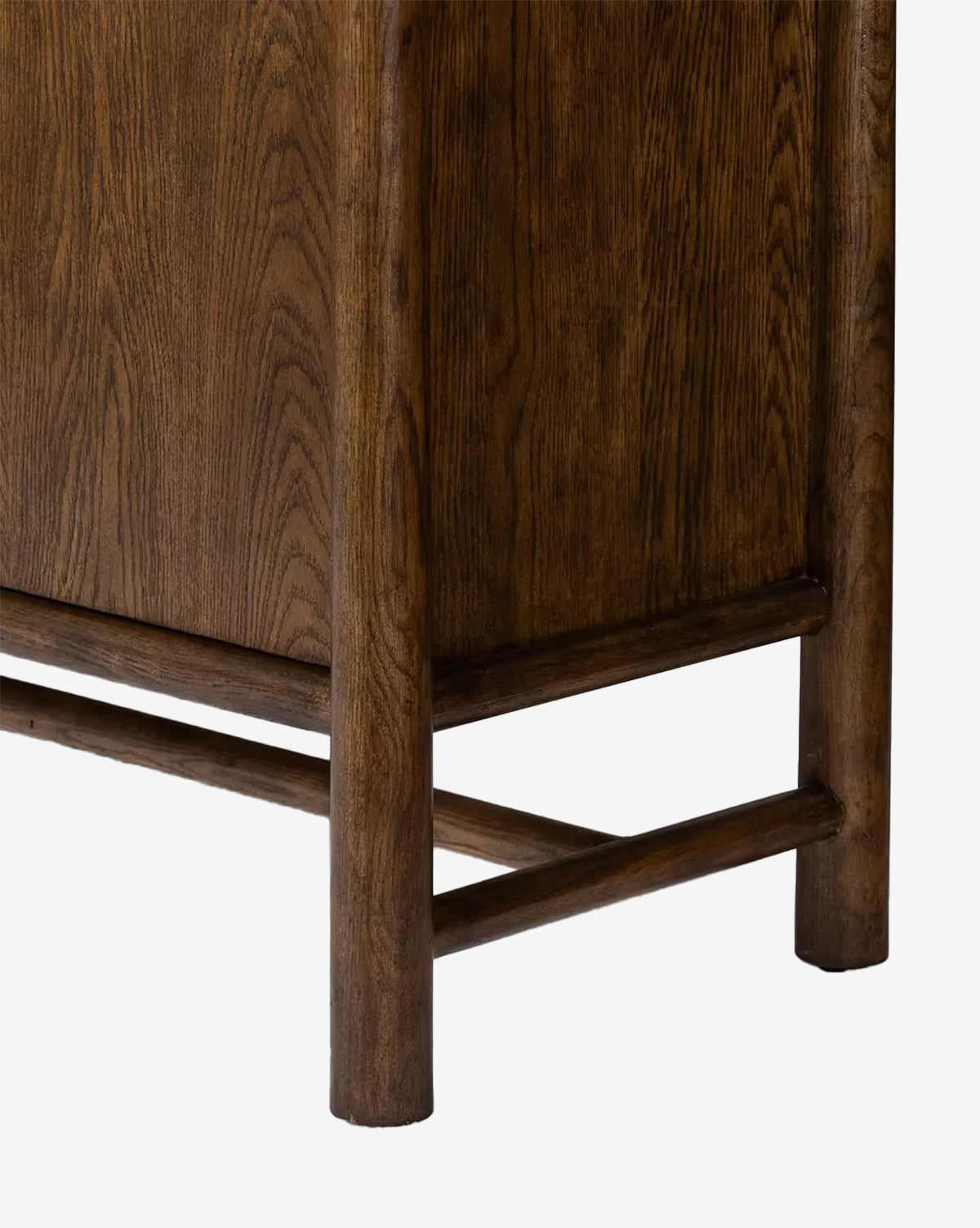 Close-up of the lower corner of the Beasley 3-Door Cabinet in dark toasted oak, featuring rounded legs, a horizontal support bar, visible wood grain, and a smooth finish that highlights its traditional elegance by McGee & Co.