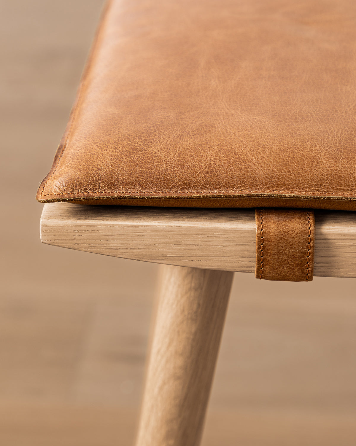 Close-up of the Beau Counter Stool, showcasing its tan leather seat cushion with a looped strap and a light, natural wood finish for a modern, refined look by McGee & Co.