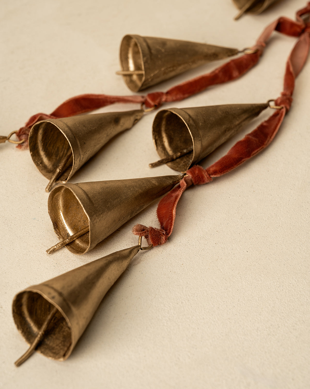 A close-up of the Bells on Velvet Ribbon Door Hanger, featuring several cone-shaped gold bells attached to velvet ribbon and displayed on a light textured surface for a charming festive accent, by McGee & Co.