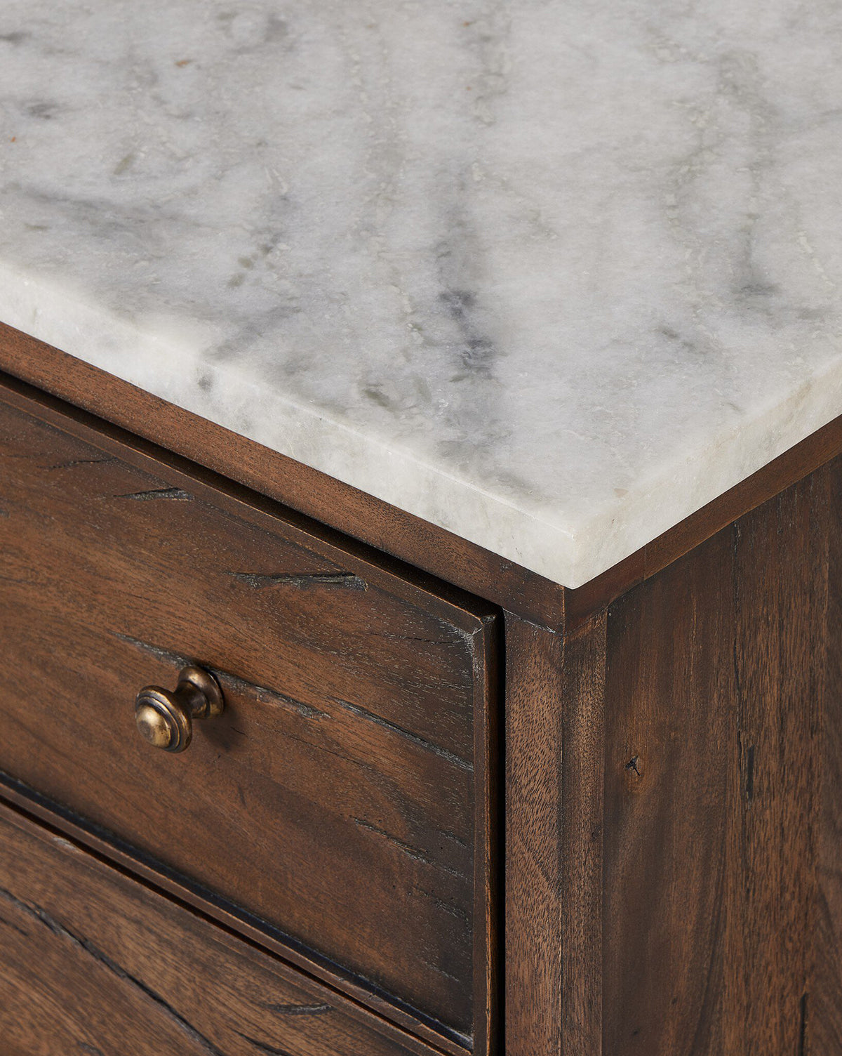 Close-up of the Bettiga Nightstand’s corner featuring a white marble top and a small round brass knob. Crafted from antique reclaimed wood, it showcases a natural, rustic finish with prominent grain and knots, by McGee & Co.