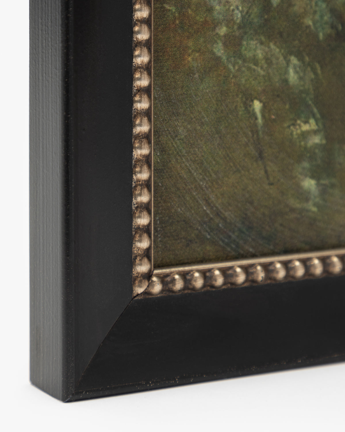 Close-up of a corner of the Blowing Brush framed giclee print, featuring a dark wooden frame with metallic beaded detailing and artwork inside that has textured green and brown tones, by McGee & Co.