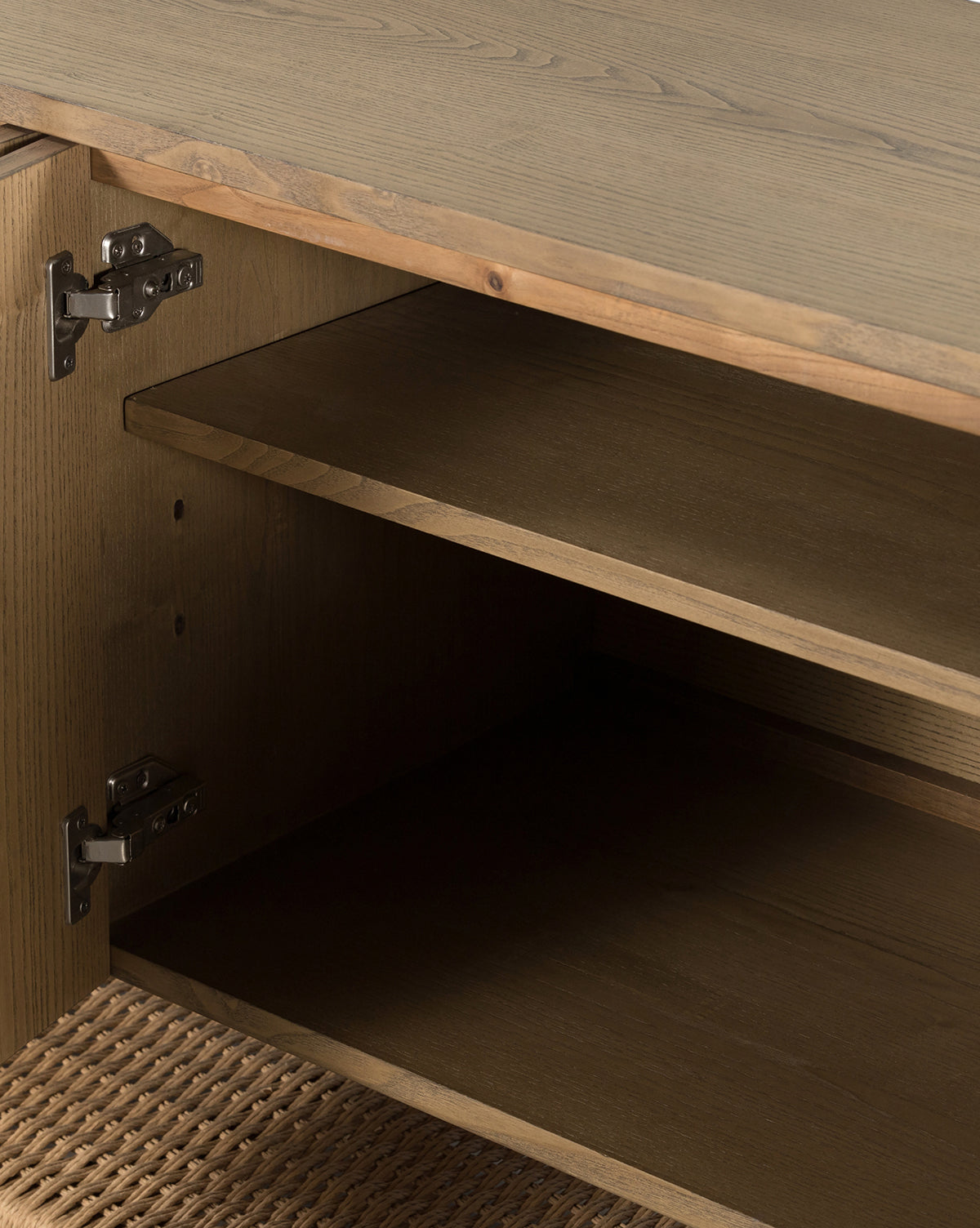 A close-up of the Brio Sideboard highlights its solid ash construction, metal hinges, open interior shelf, and woven rattan base—an elegant example of refined Danish design, by McGee & Co.