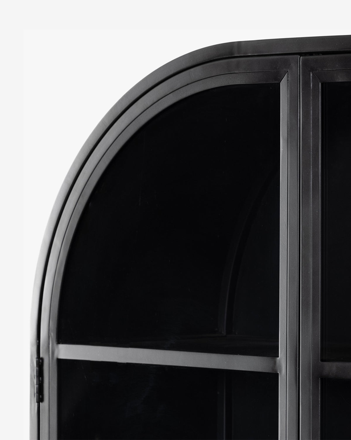 Close-up of the Brookes Cabinet’s upper corner, highlighting its smooth arched top and sleek black iron frame with elegant rectangular glass door panes, by McGee & Co.