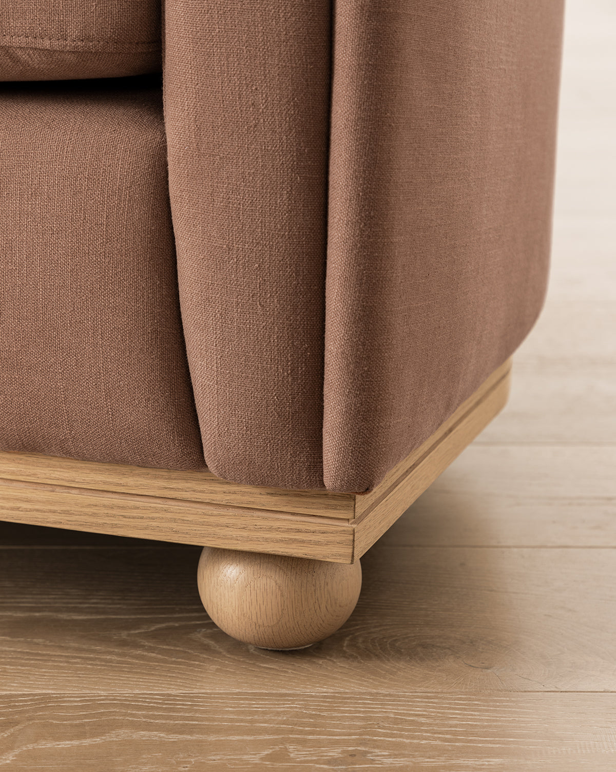 Close-up of the Bunnell Lounge Chair (Ready to Ship) corner, highlighting its textured dusty rose upholstery, light wooden base, and rounded leg—a modern traditional chair on light wood flooring, by McGee & Co.