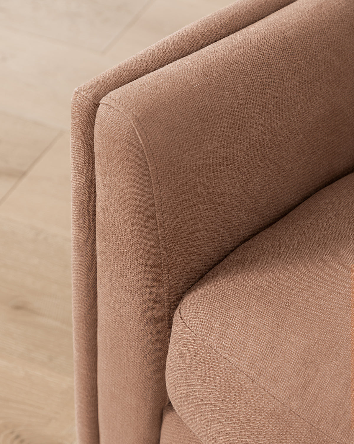 Close-up of a corner of the Bunnell Lounge Chair (Ready to Ship), a modern traditional piece in light brown fabric with cushioned armrest and seat, shown on a light wooden floor, by McGee & Co.