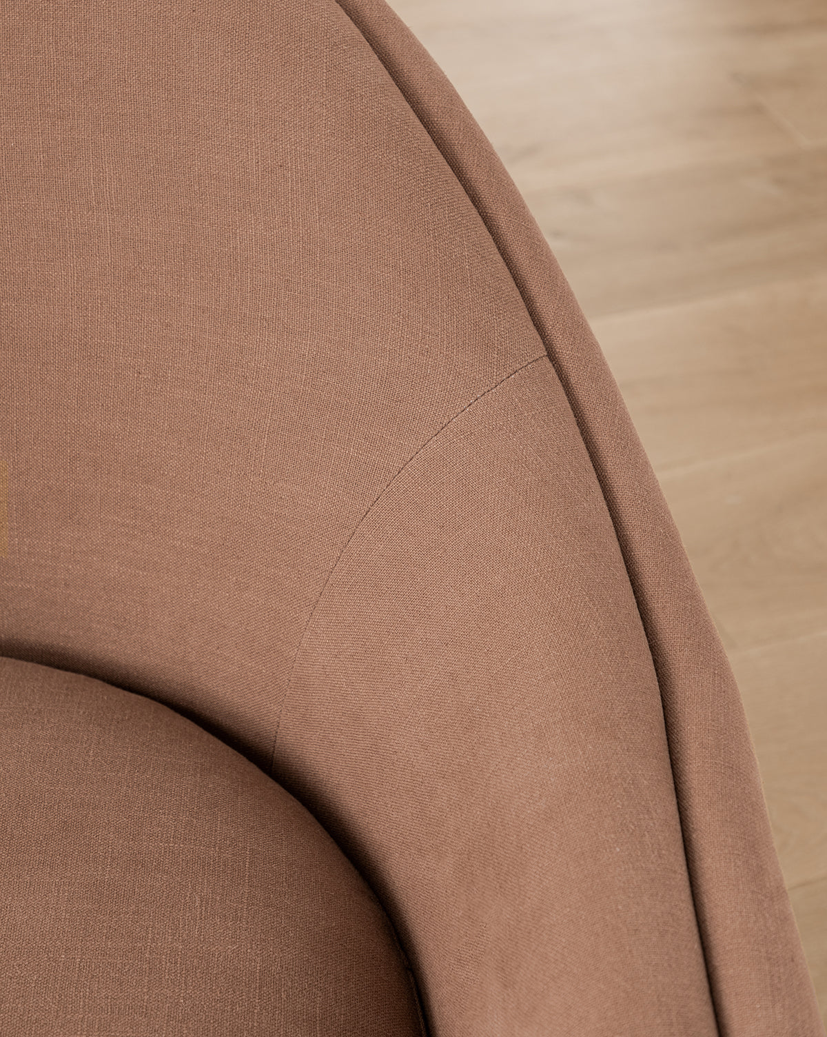 Close-up of the curved armrest and backrest of the Bunnell Lounge Chair (Ready to Ship), a modern-traditional chair in brown fabric upholstery, with wooden flooring visible in the background by McGee & Co.