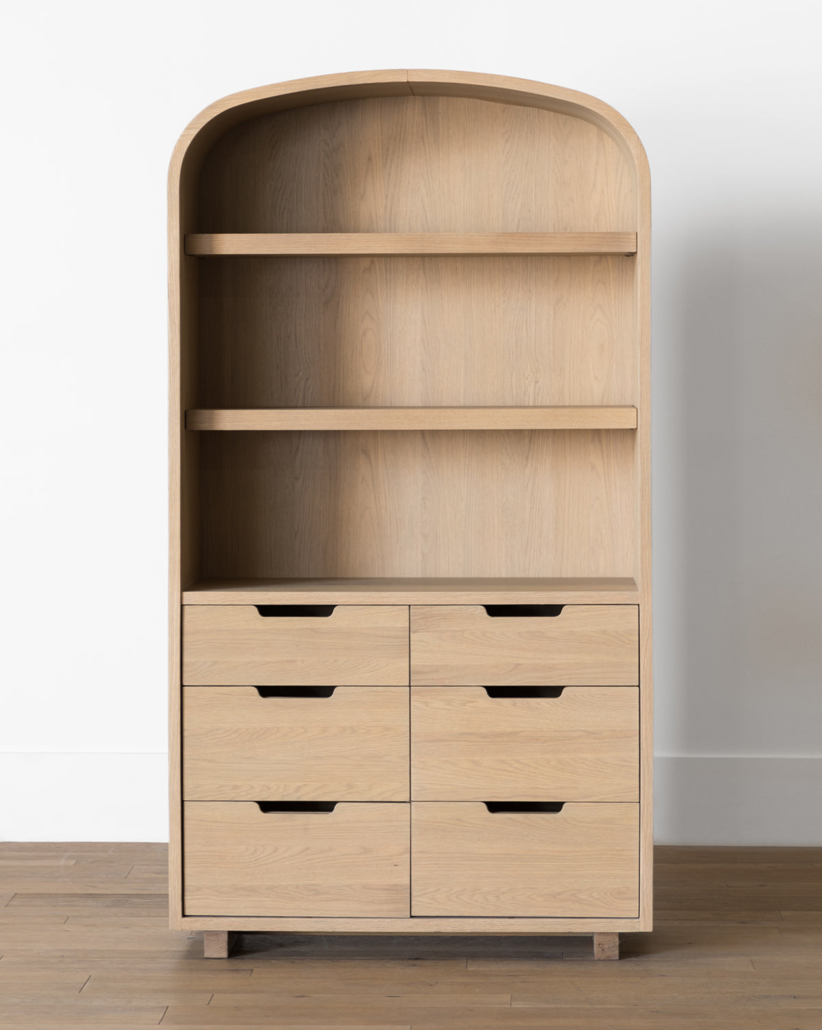 The Burnham Cabinet features a light oak finish, arched top, two open shelves, and six drawers with cut-out handles—ideal for adding stylish storage to your dining room against a white wall and wooden floor, by McGee & Co.