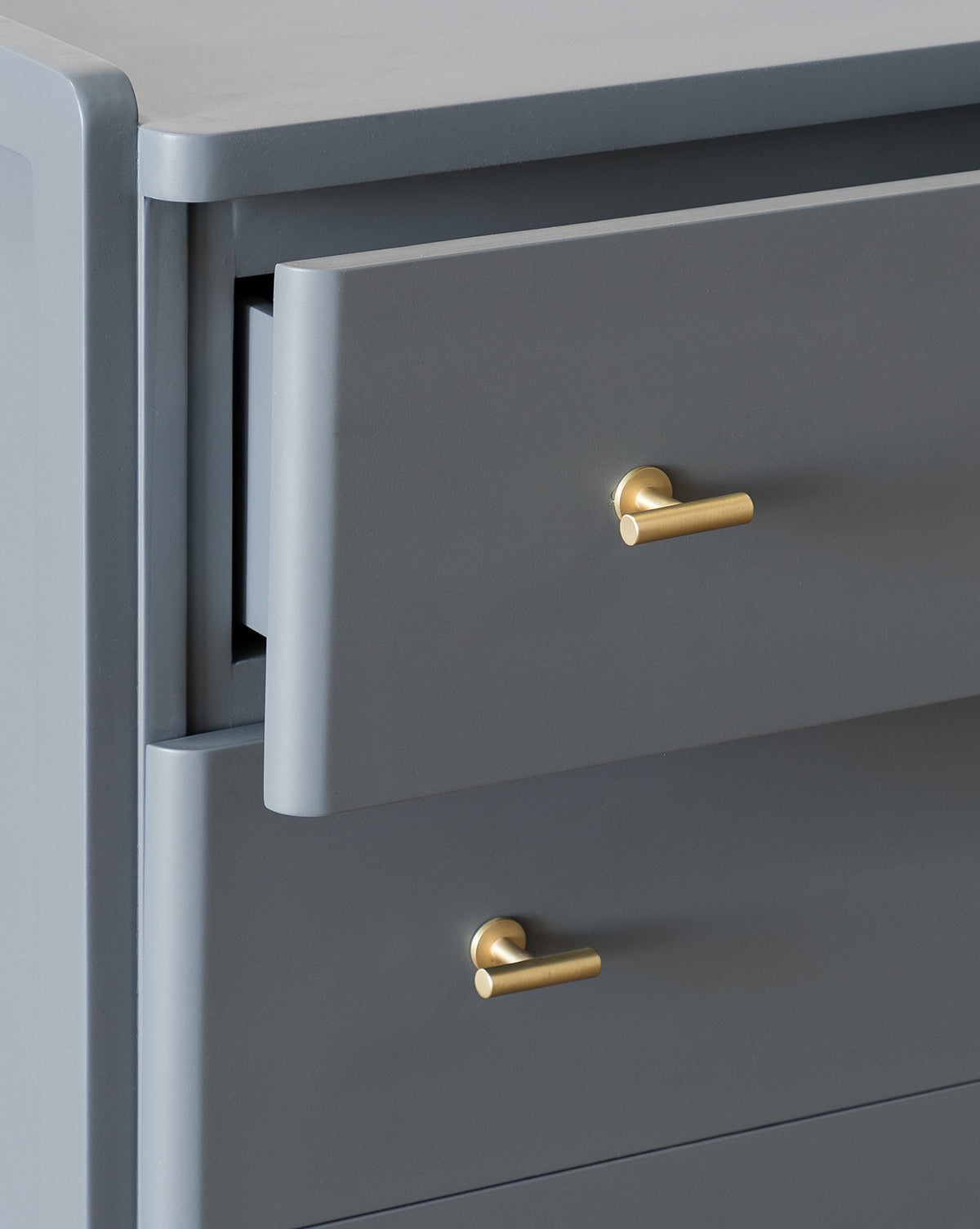 A close-up of the Butler Dresser in slate blue shows gold handles and one slightly open top drawer. Featuring a smooth matte finish and clean, minimalist lines, this modern dresser has the rest of its drawers closed, by McGee & Co.