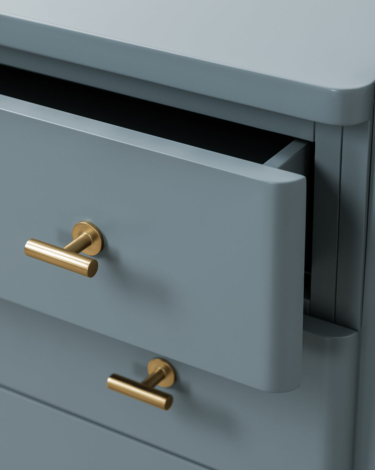 A close-up of the Butler Nightstand in slate blue features sleek gold handles. One drawer is partially open, showing its empty interior. The smooth surface and modern edges blend classic style with contemporary design, by McGee & Co.