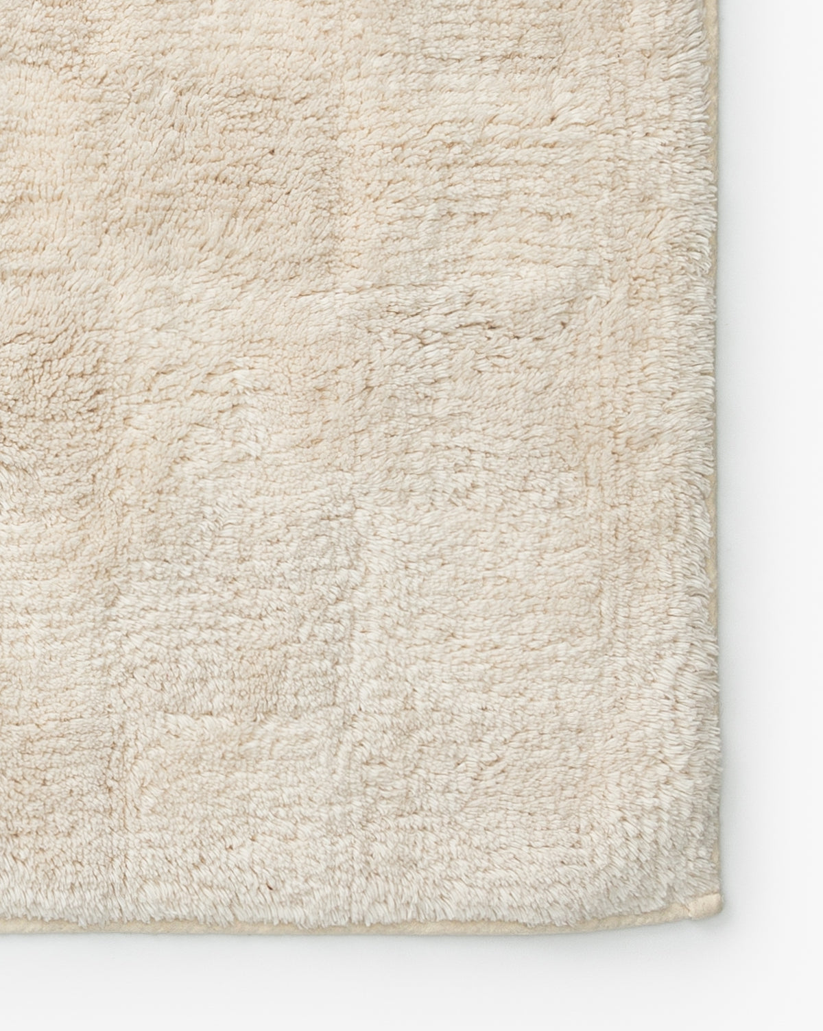 A close-up of the Callen Bath Mat’s corner shows its soft, cream-colored cotton fabric and subtle textured pattern.