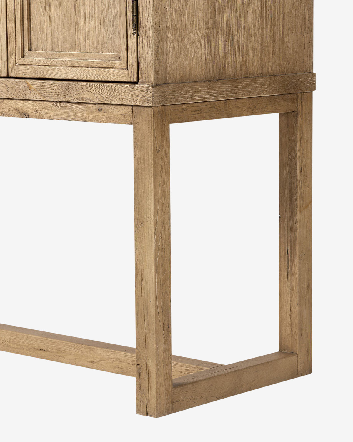 Close-up of the Carrington Cabinets lower corner, highlighting its rectangular frame base, worn oak wood grain, and minimalist design against a white background, by McGee & Co.