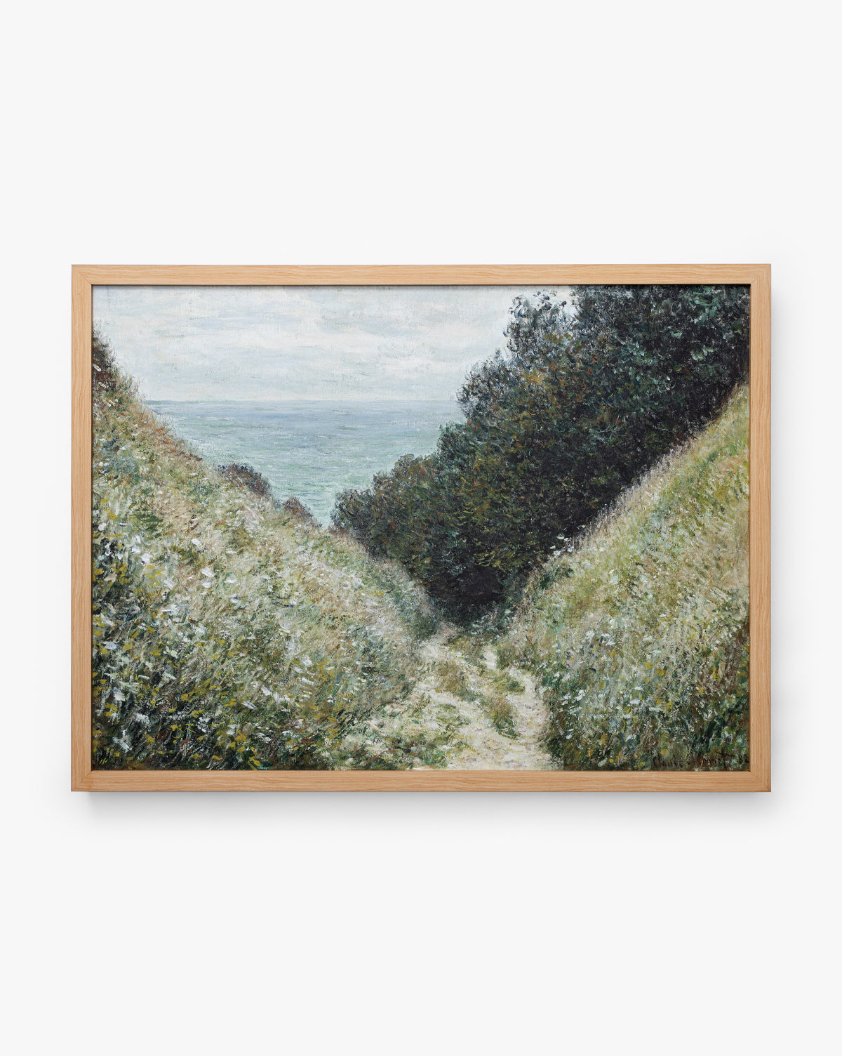 Carved Path is a giclee on canvas in a natural oak frame, showing a tranquil scene: a winding path between green hills leads to misty water below cloudy skies, with dense foliage flanking the route, by McGee & Co.