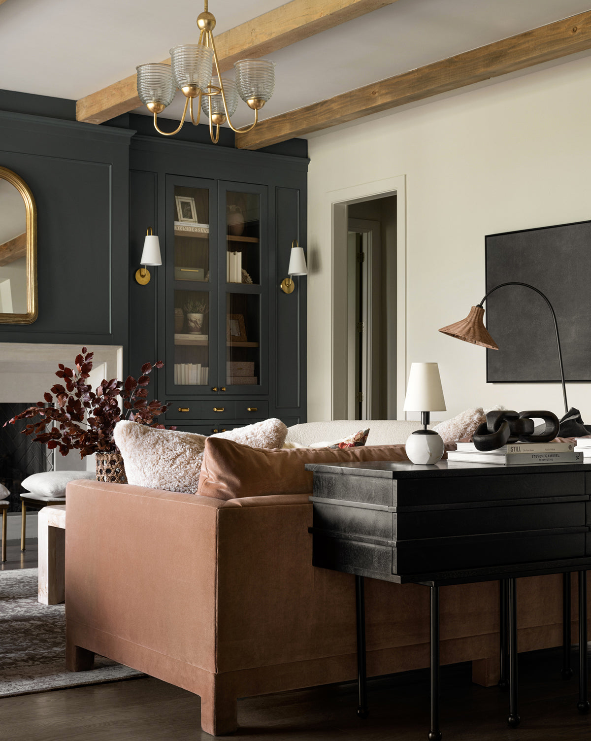 A modern living room features a blush velvet sofa, dark built-ins, wood ceiling beams, a neutral rug, decorative lighting including the Tiny Terri Accent Lamp with a natural paper shade, and a blend of minimalist and classic furnishings by McGee & Co.
