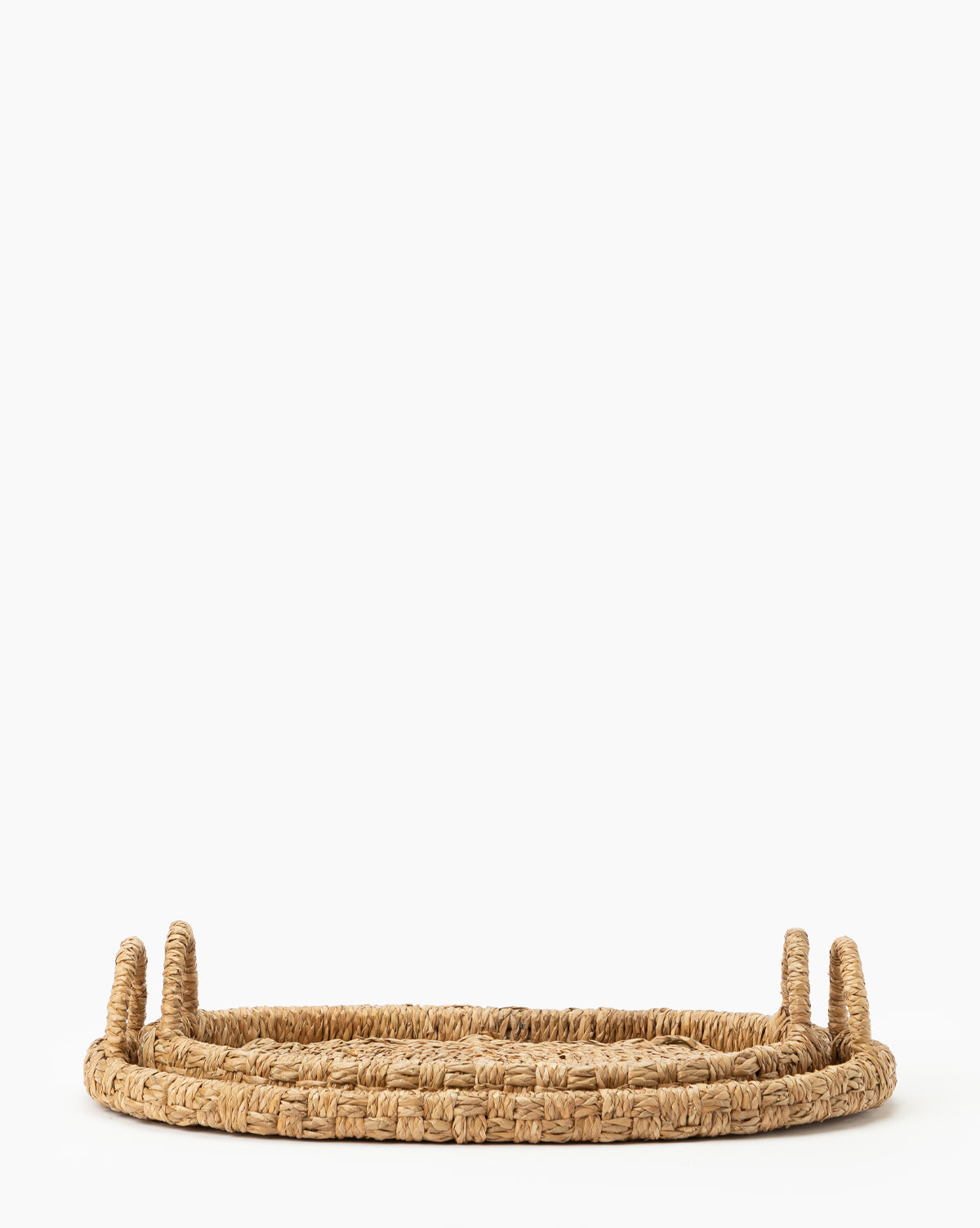 The Celia Woven Tray (Set of 2) features flat, oval hand-woven seagrass trays with two looped handles, ideal for use as coffee table trays and shown against a plain white background, by McGee & Co.