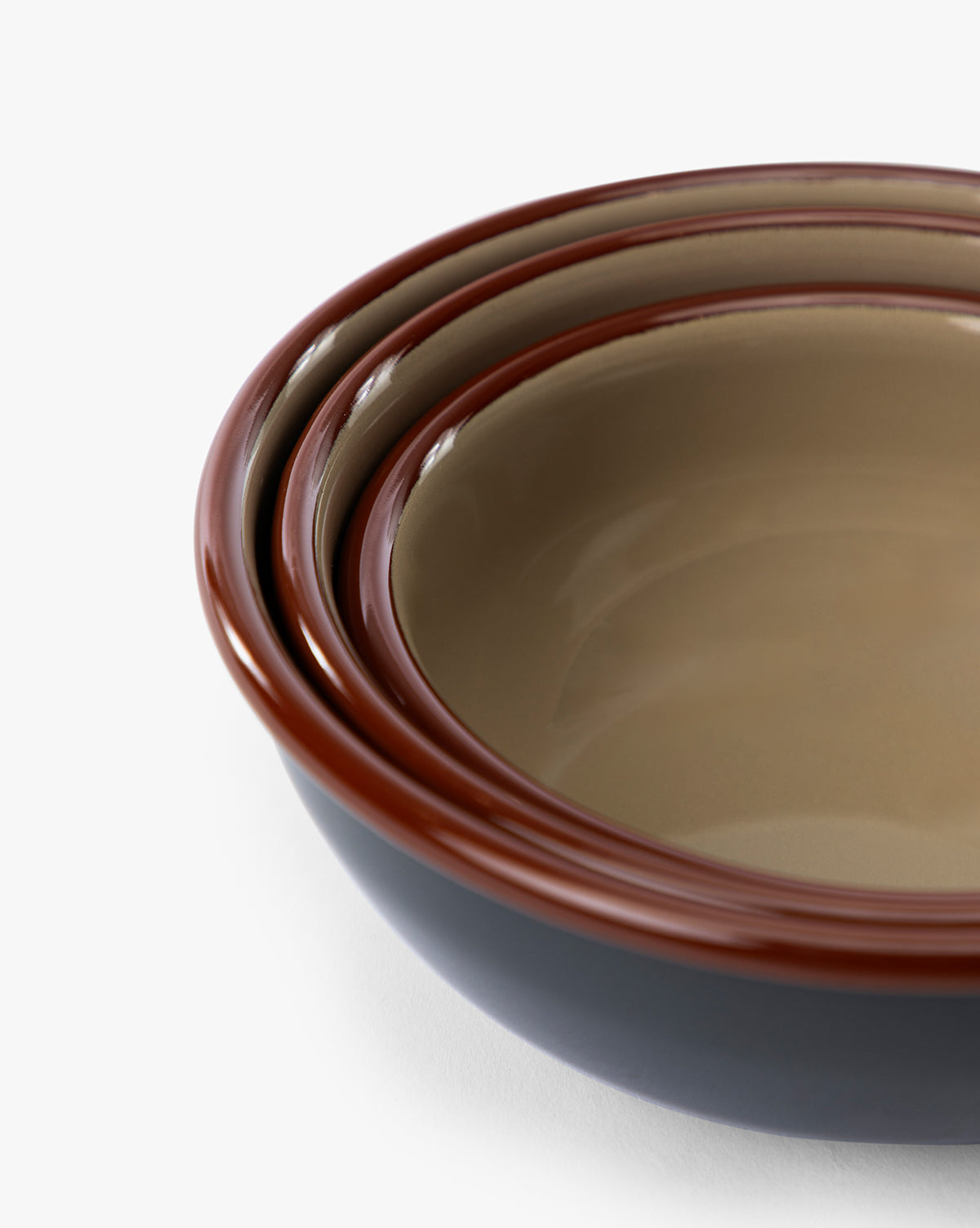 The Charles Enamel Bowls (Set of 3) features eco-friendly, nested bowls in varying sizes with beige interiors, dark exteriors, and reddish-brown rims. The angled image highlights their inner sides and distinctive rims by McGee & Co.