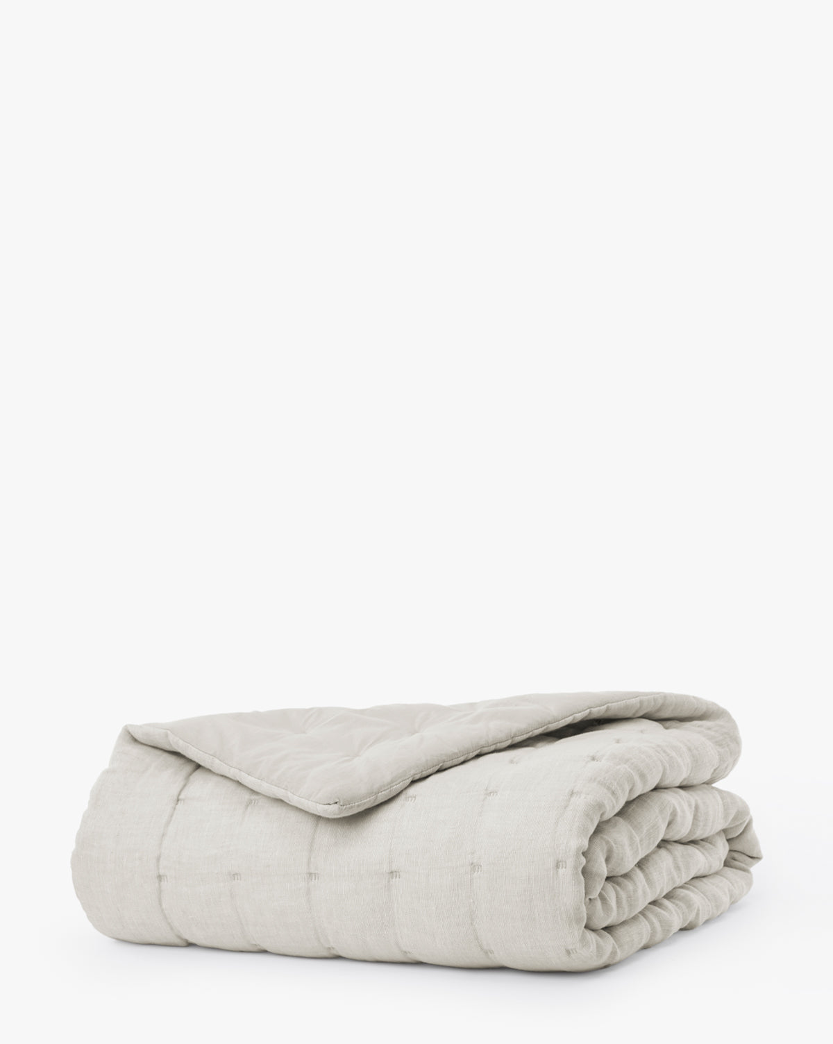 The Chaucer Quilt, in light gray with quilted stitching and a subtle grid pattern, is neatly folded and displayed against a plain white background.