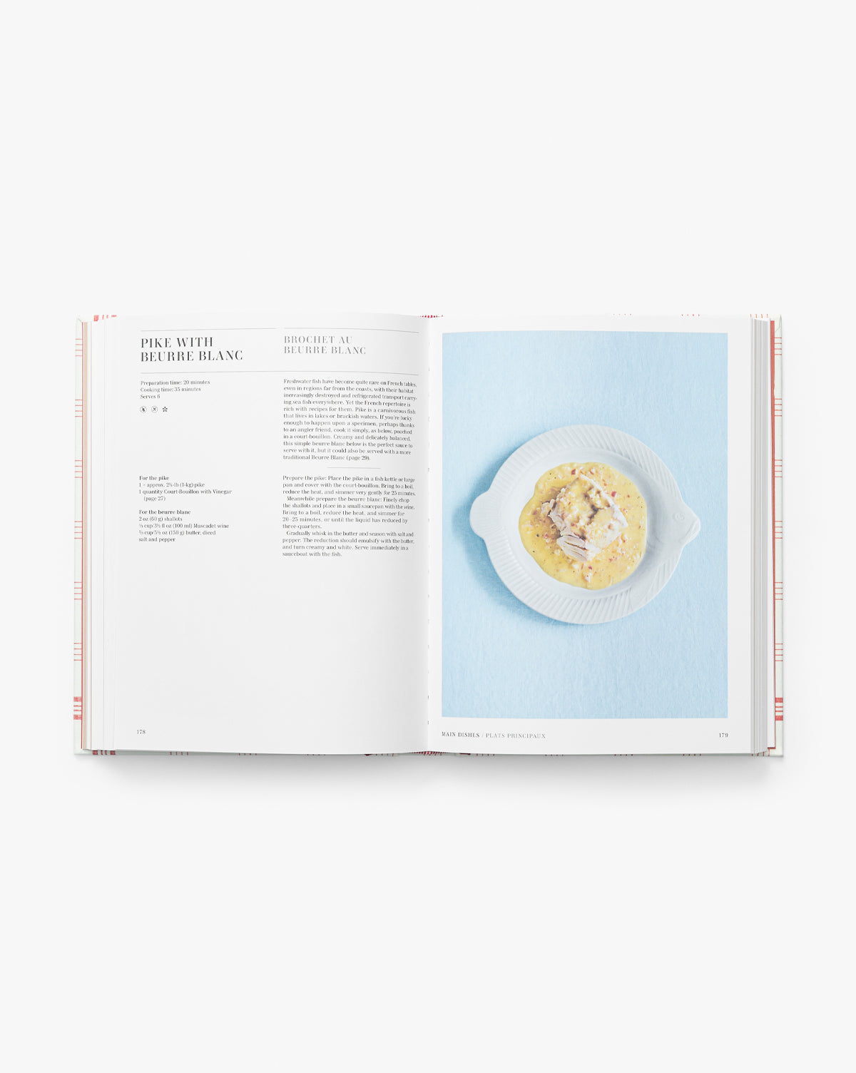 An open Classic French Recipes cookbook lies against a light blue background, featuring a Pike with Beurre Blanc recipe on the left page and a photo of the finished dish on the right, by McGee & Co.
