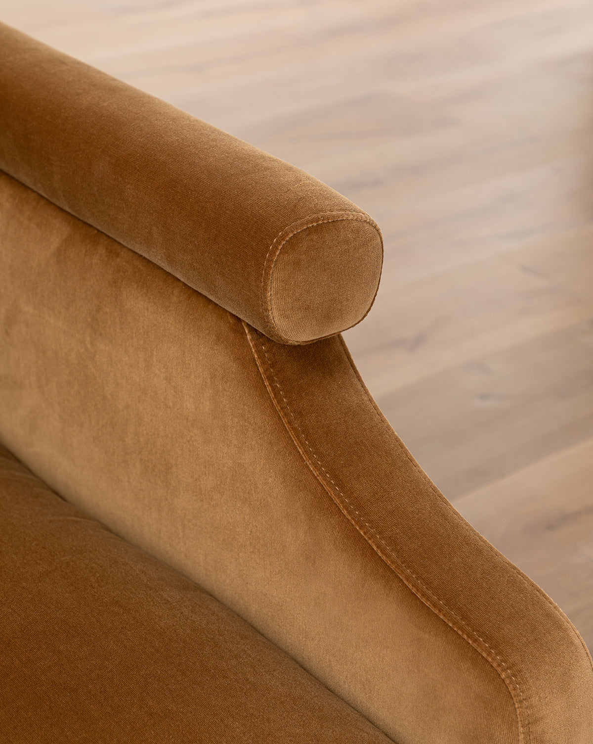 Close-up of the Clegg Lounge Chair’s brown cotton velvet armrest with a rounded top, set against a light wooden floor, by McGee & Co.