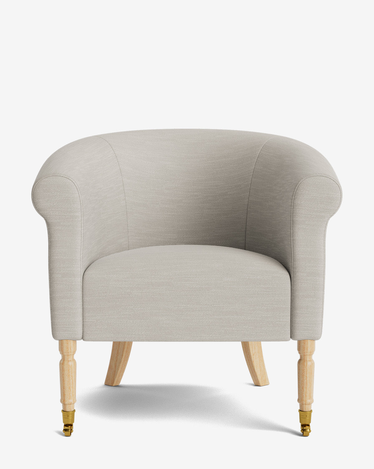 The Clemence Lounge Chair features light grey designer fabric upholstery, rounded arms and backrest, light wood legs, and small brass casters on the front two legs, shown against a plain white background by McGee & Co.