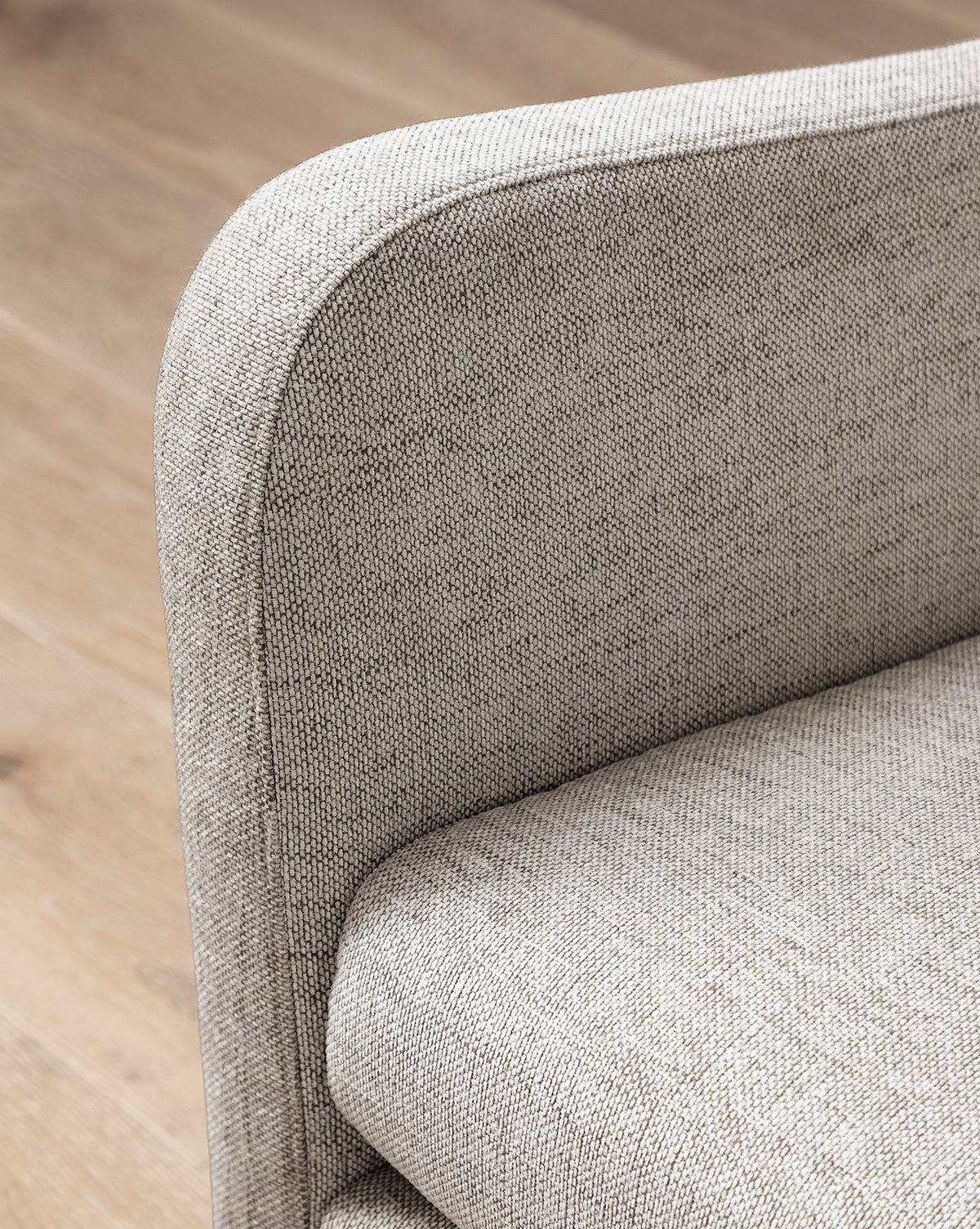 Close-up of the Commodore Settee 68, a modern, light gray deep-seated sofa with rounded armrest and soft seat cushion in twine Crypton upholstery, placed on a light wooden floor by McGee & Co.