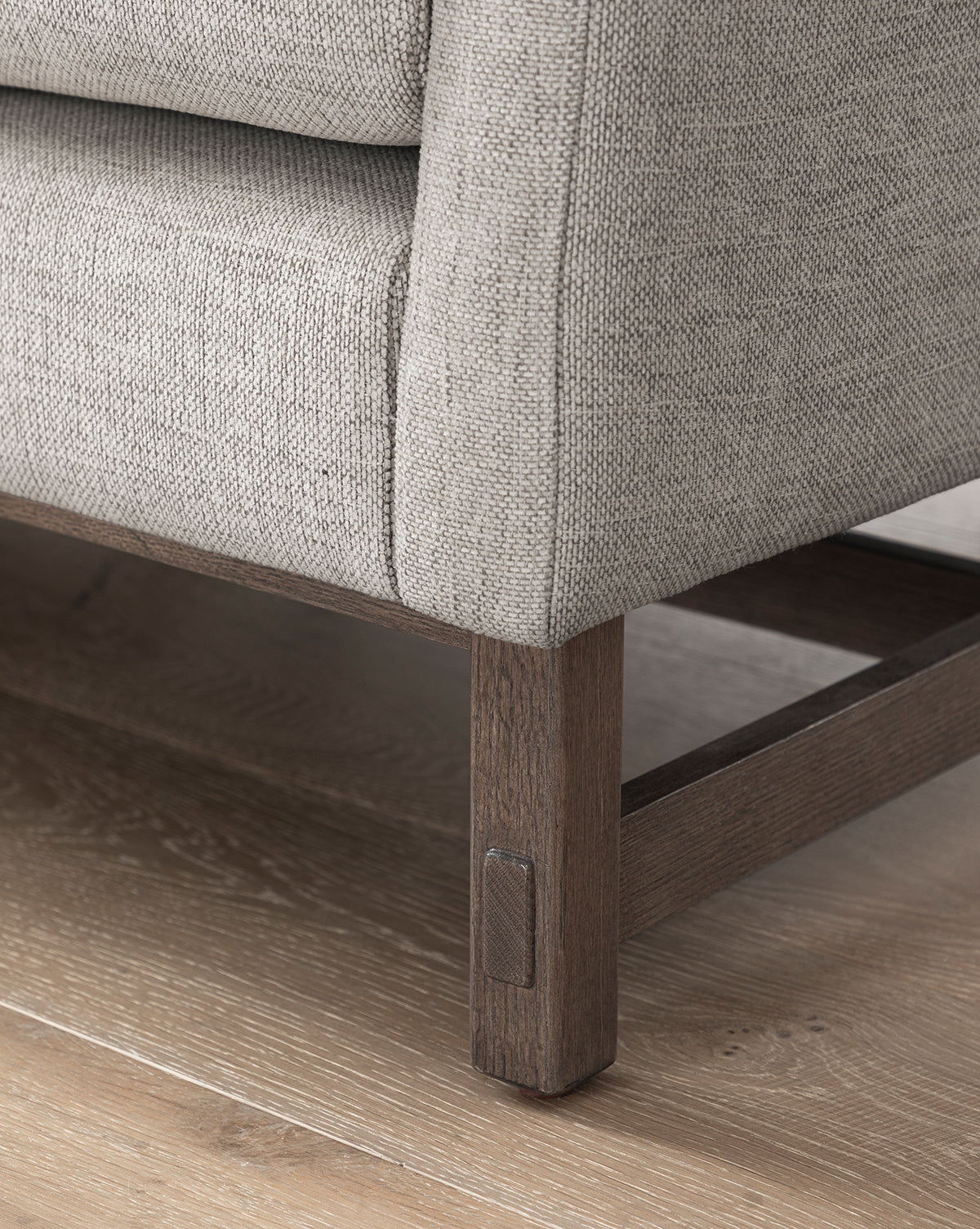 Close-up of the Commodore Settee 68 in light gray twine Crypton upholstery, featuring a deep seat and dark brown stained wooden frame with square legs. The textured weave fabric contrasts beautifully with the wood base on light flooring, by McGee & Co.
