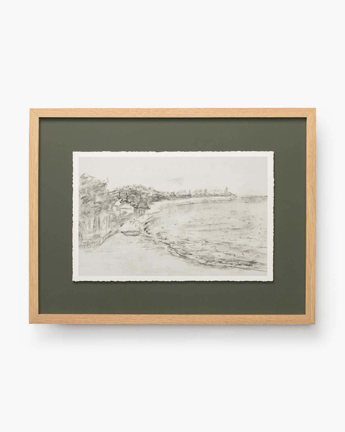 Cove in Charcoal: Framed charcoal sketch of a coastal landscape with a curved shoreline, sea, trees, and distant buildings under a cloudy sky. Mounted on a green mat in a light oak frame—an elegant touch for any home decor, by McGee & Co.