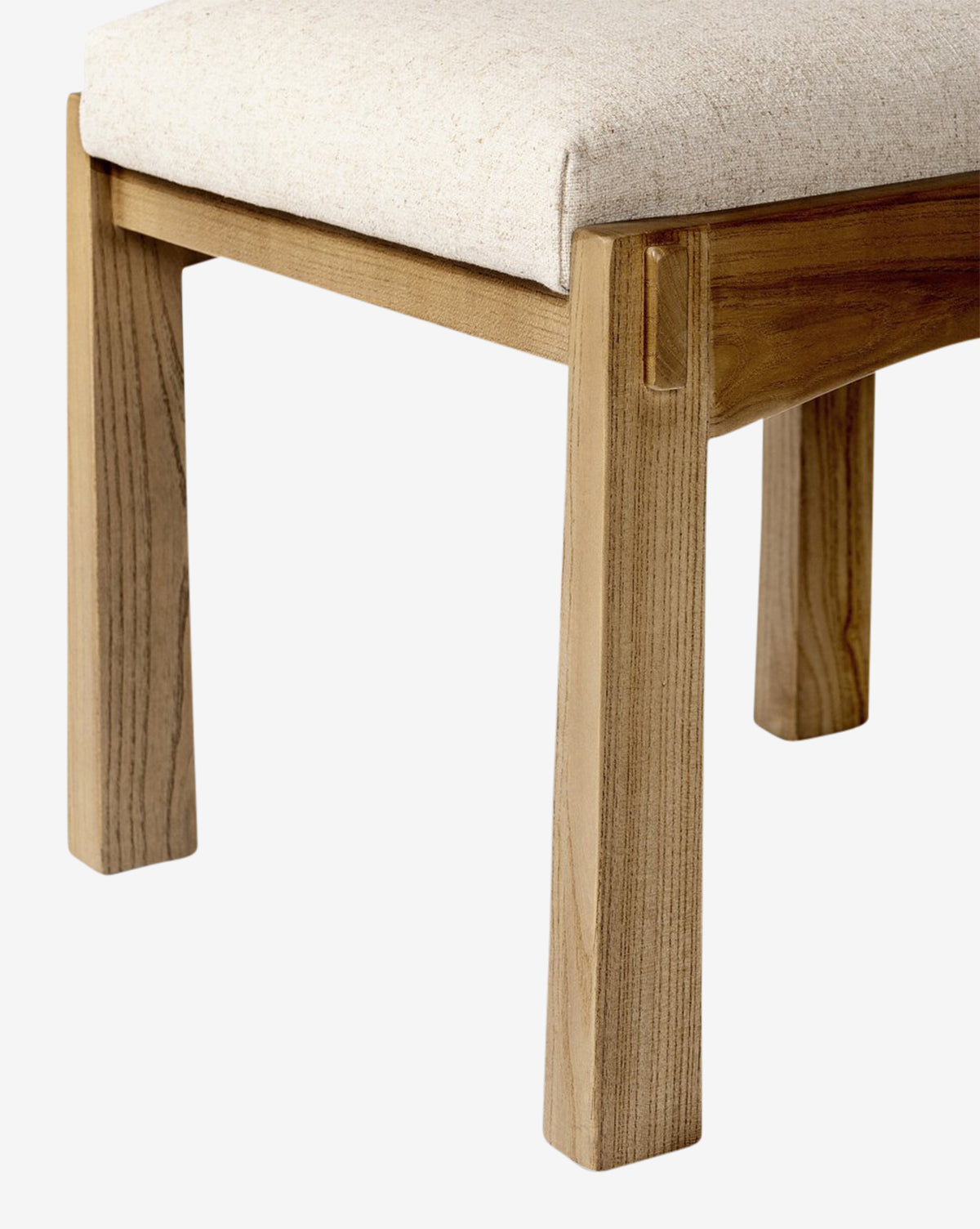 A close-up of the Cyprian Dining Chair’s natural wood frame and leg with a light performance fabric seat, highlighting the wood grain against a white background, by McGee & Co.