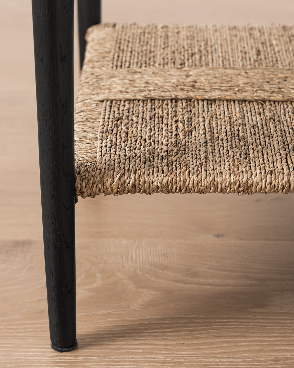 Close-up of the Dana Nightstand, featuring a woven seagrass shelf supported by a black metal frame and placed on a light wood floor, by McGee & Co.