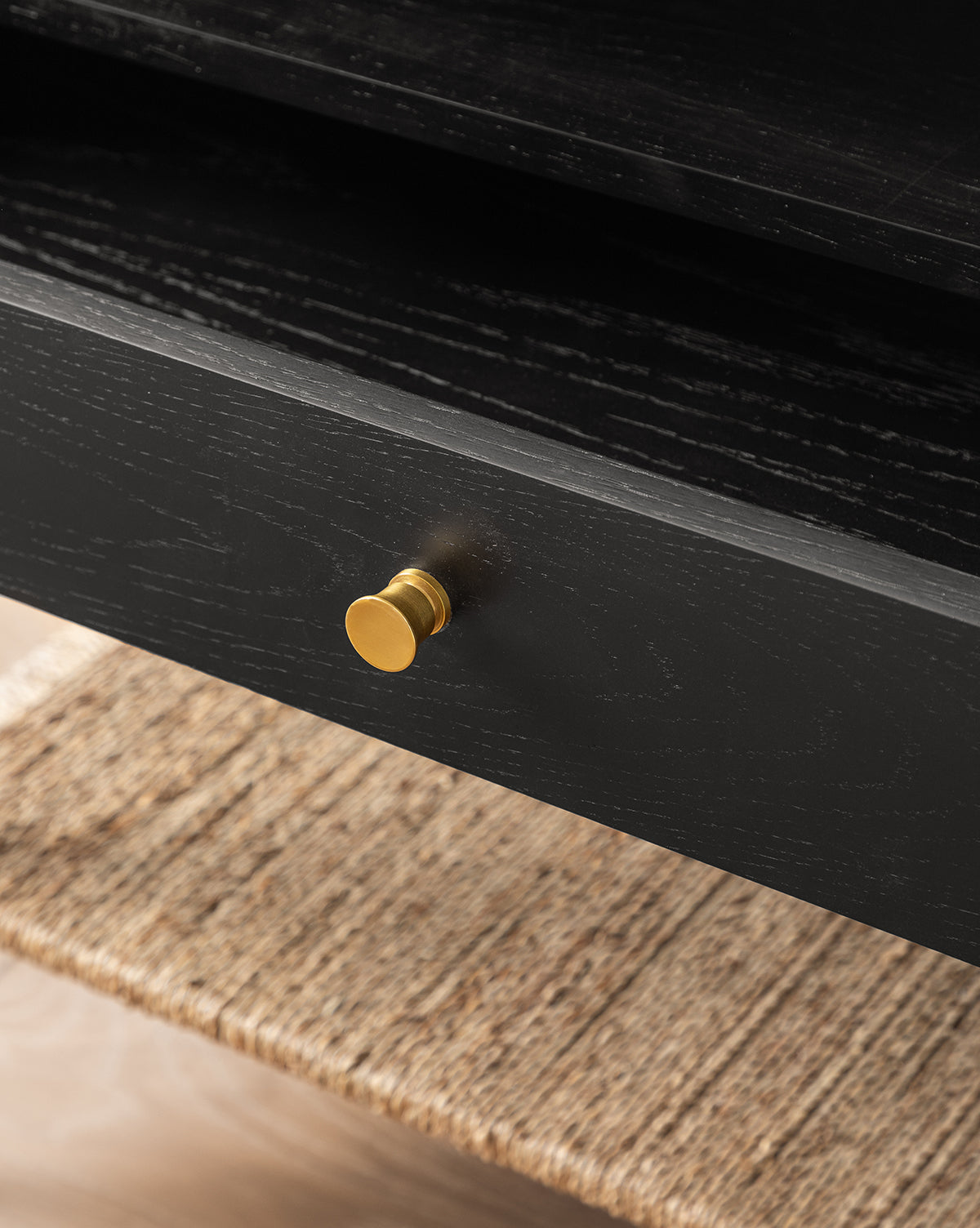 Close-up of the Dana Nightstand in black oak, showcasing a round gold knob and a woven seagrass shelf beneath the partially open drawer by McGee & Co.